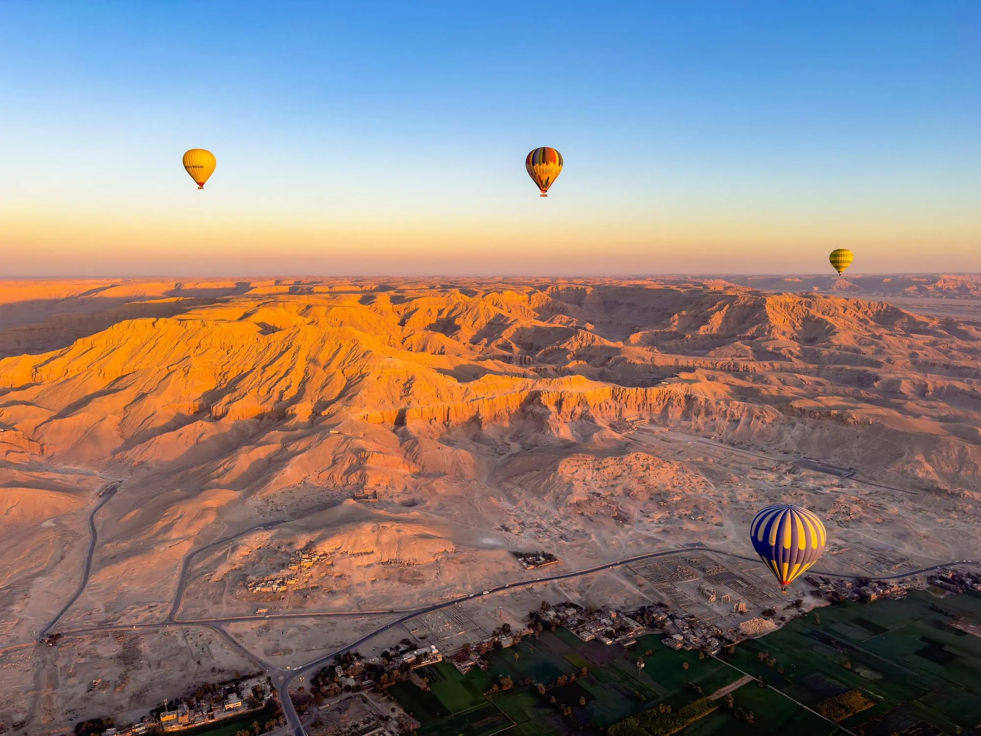 Aerial view of Valley of the Kings with hot air balloons floating over desert cliffs and ancient tombs