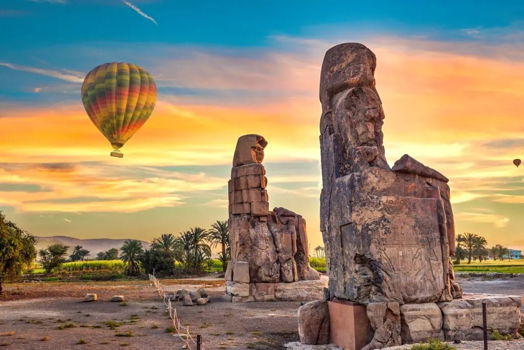 Hot air balloons rising near the Colossi of Memnon at sunrise with the west bank landscape in view, Luxor