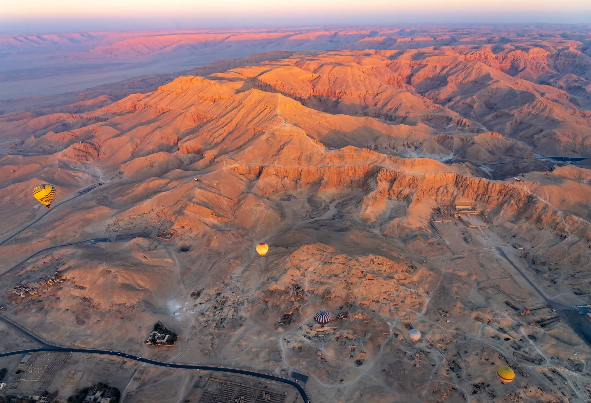 Aerial view of Valley of the Kings with hot air balloons floating over ancient ruins and desert mountains in Luxor, Egypt