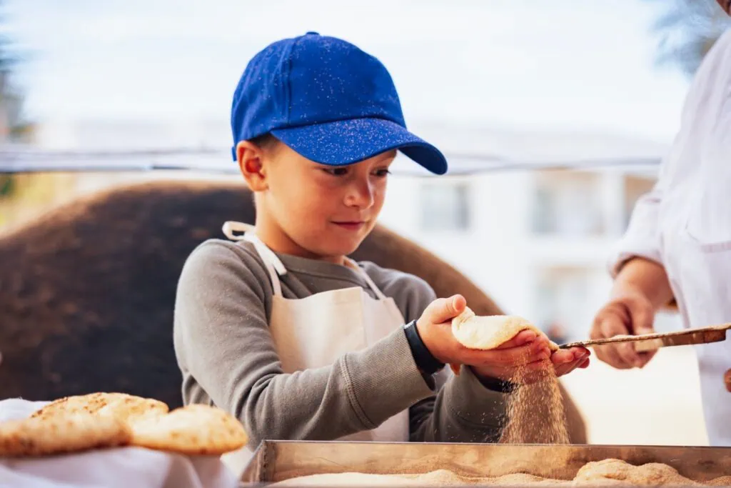 Child shaping traditional Egyptian bread dough in a local bakery setting