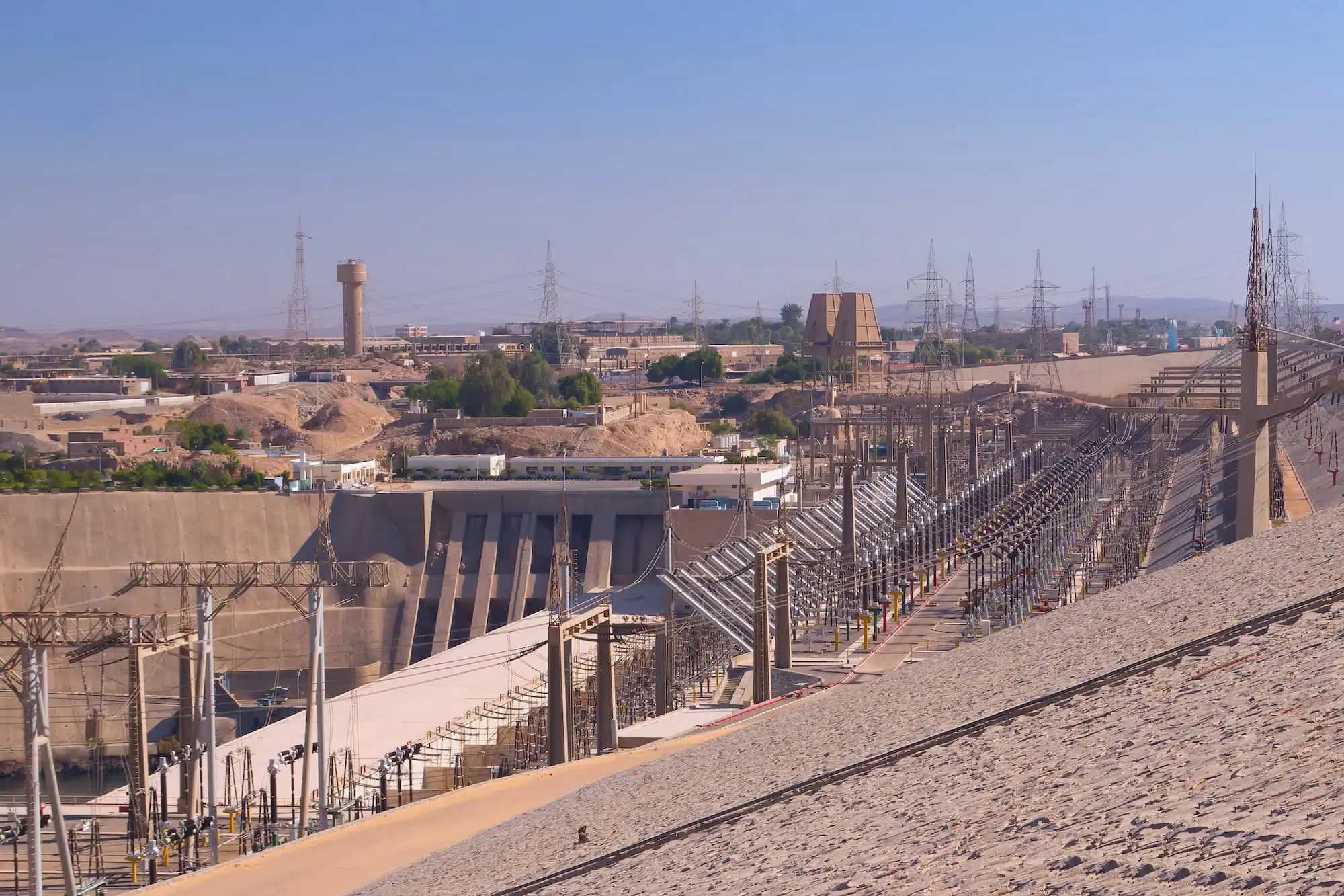Aswan High Dam concrete structure with power transmission towers in Egyptian desert