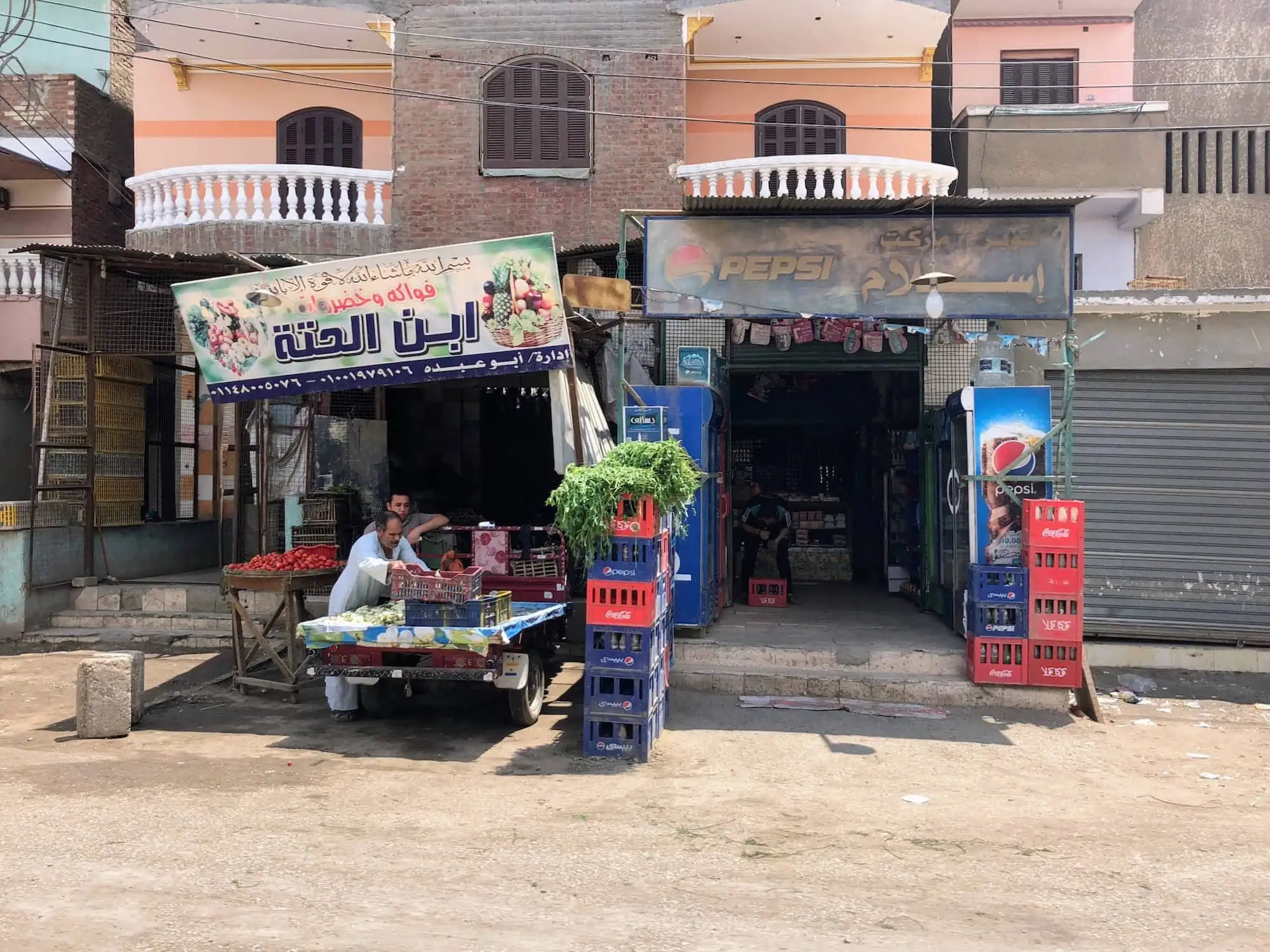 Egyptian street vendor selling vegetables and fruits with international beverage brands visible