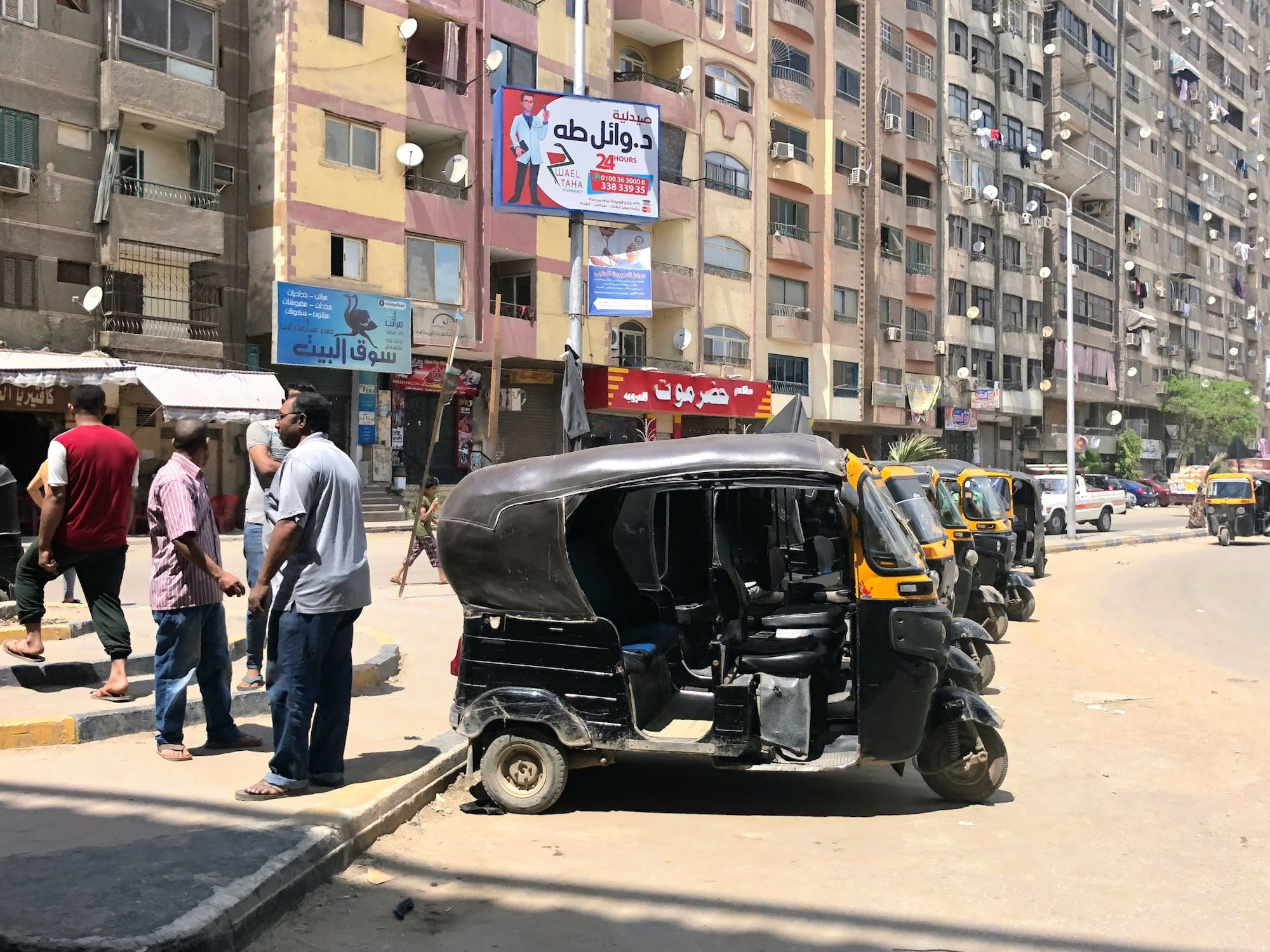 Busy Egyptian street with tuk-tuk, apartment buildings and Arabic commercial signage