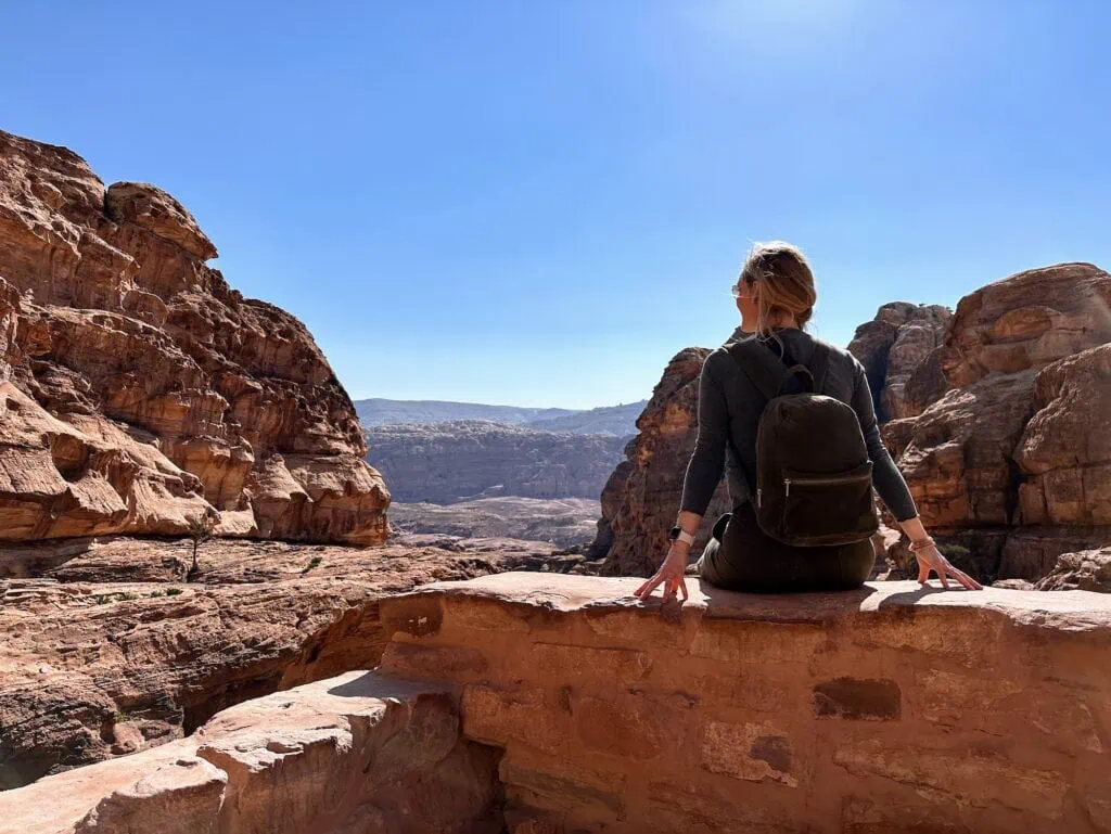 Female tourist sitting on a rock overlooking the Petra archaeological site from above Wadi Musa
