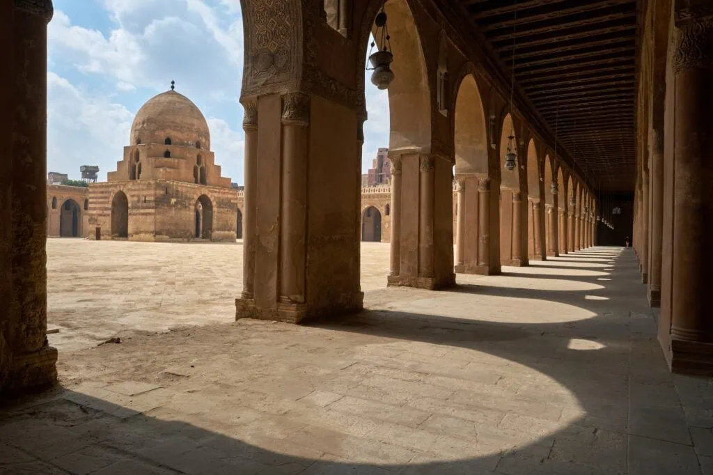 An exterior view of the vast courtyard, brick arcades, and spiral minaret of the Ibn Tulun Mosque, Cairo
