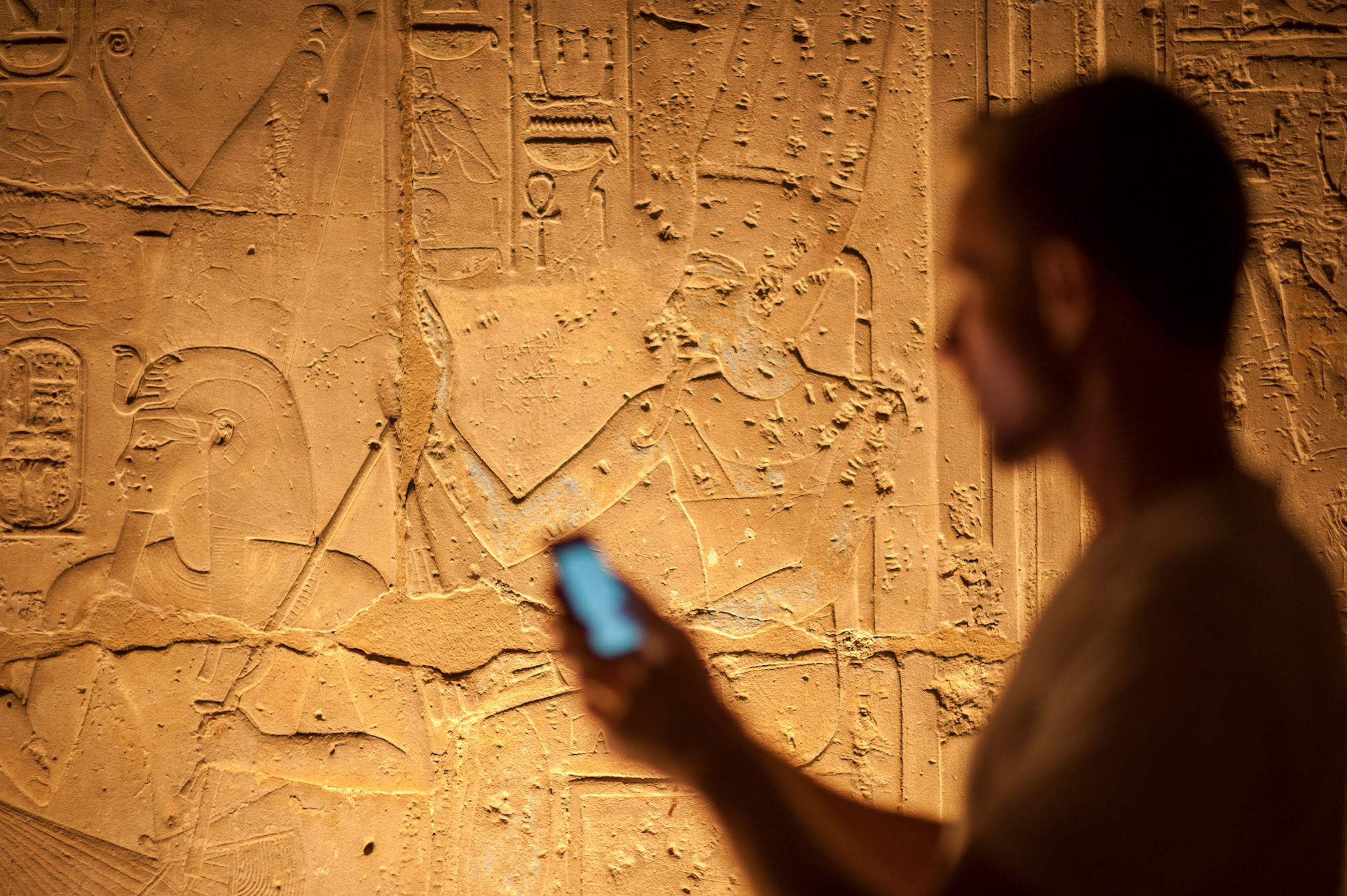 Person using smartphone to document ancient Egyptian hieroglyphic carvings on stone wall