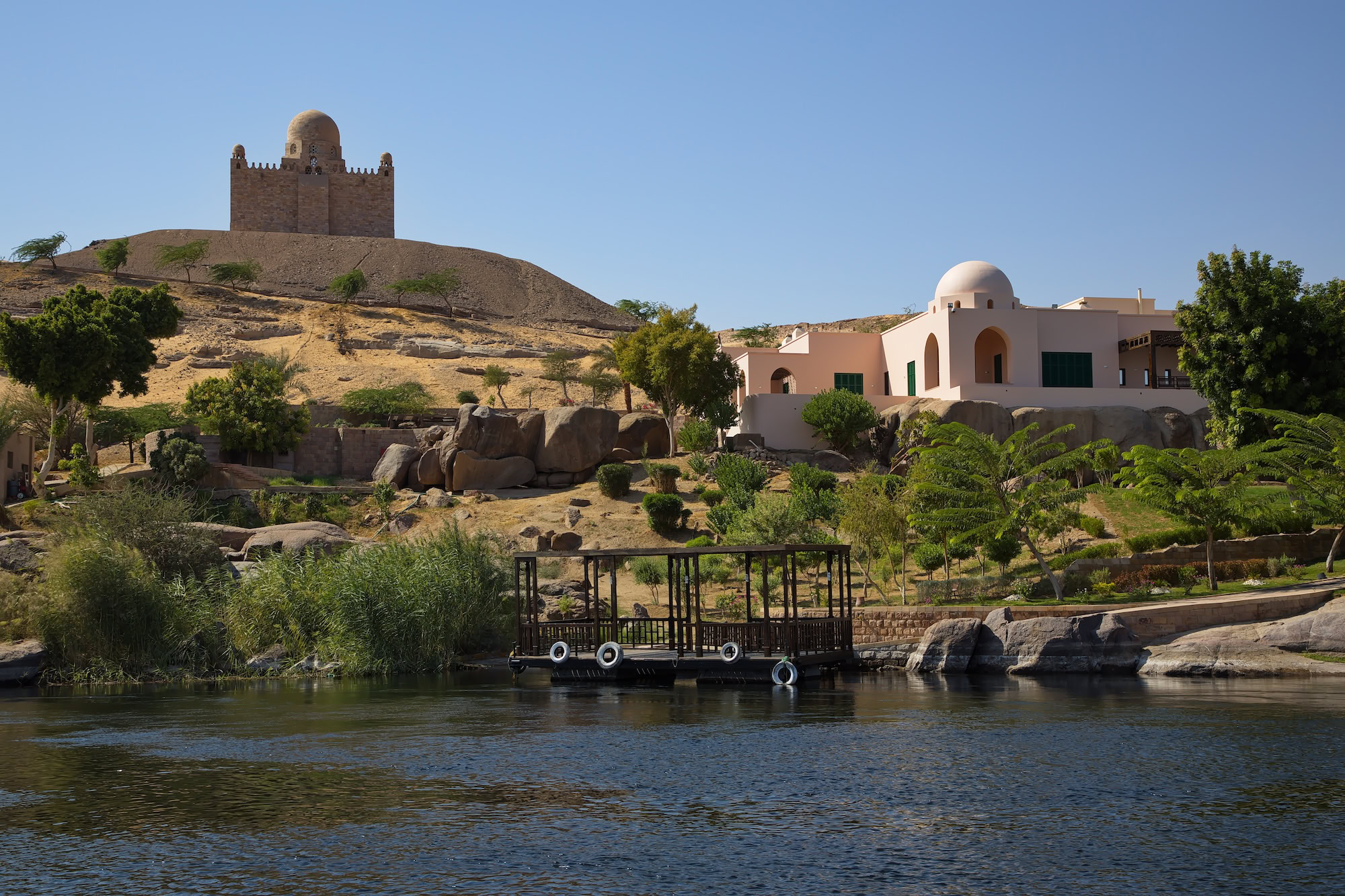 Wooden jetty extending into the Nile River at Aswan with granite boulders and sandy terrain