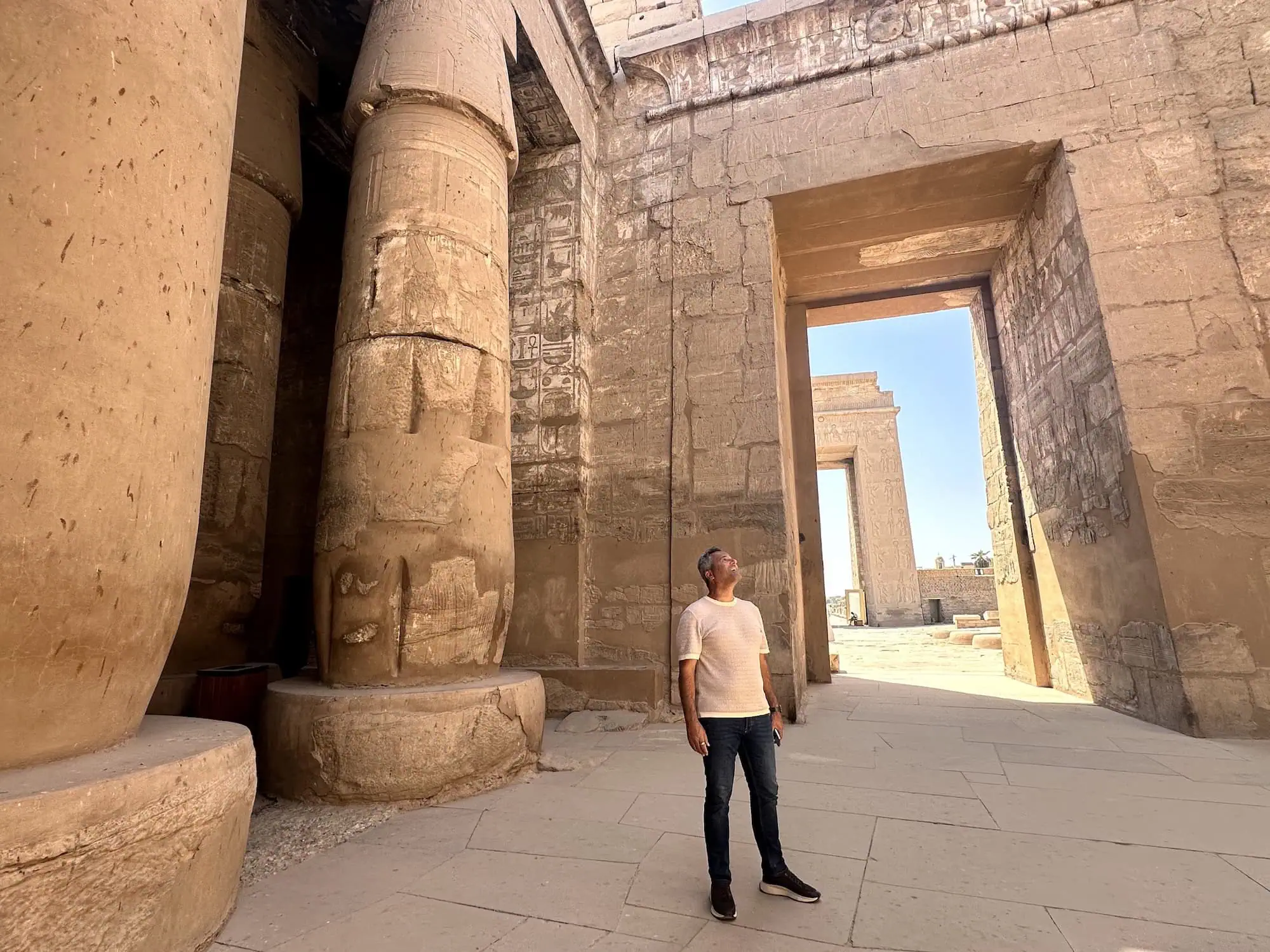 Man standing inside Karnak Temple complex looking up at massive stone columns with hieroglyphic carvings
