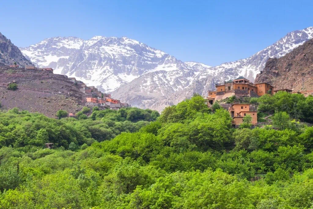 Kasbah du Toubkal with stone buildings set on a hillside overlooking terraced valleys and mountain peaks, Imlil