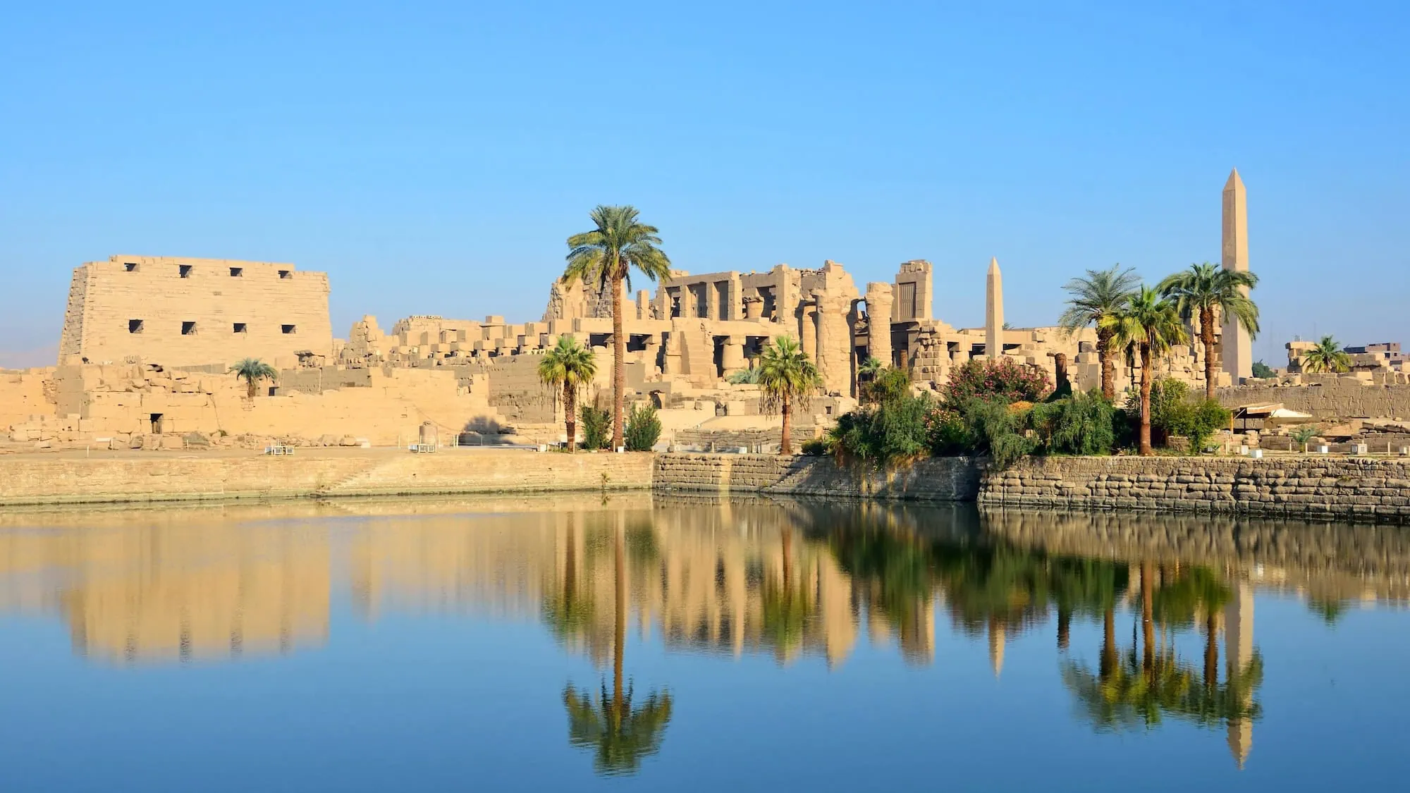 Karnak Temple complex with obelisk and palm trees reflected in water