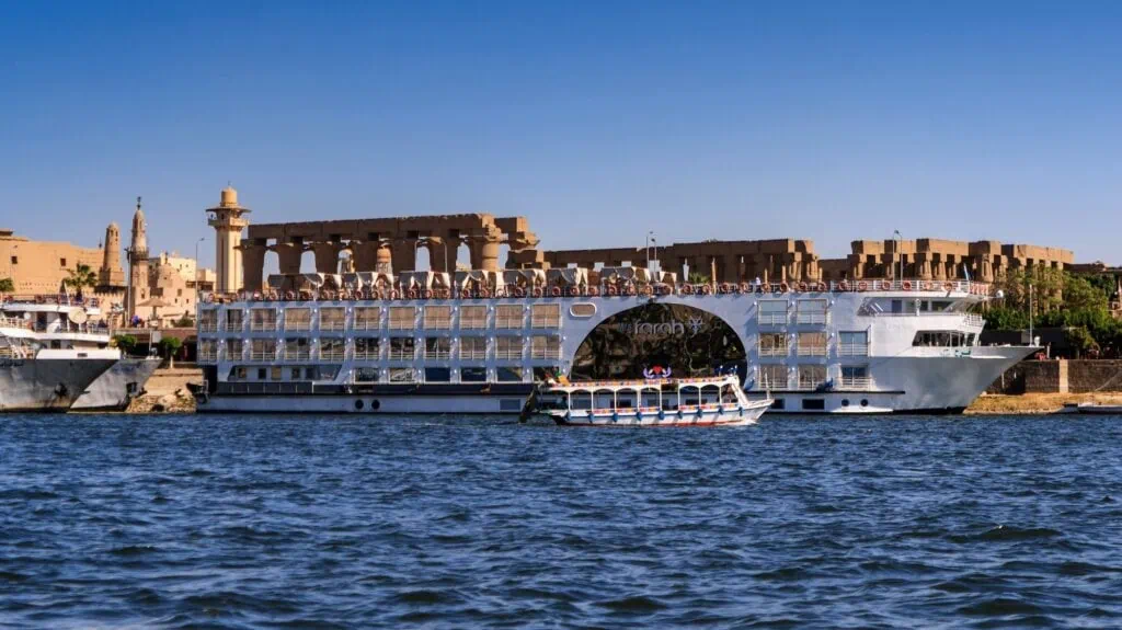 Love Boat passing the cruise liner Farah moored along the Nile River riverbank, Luxor