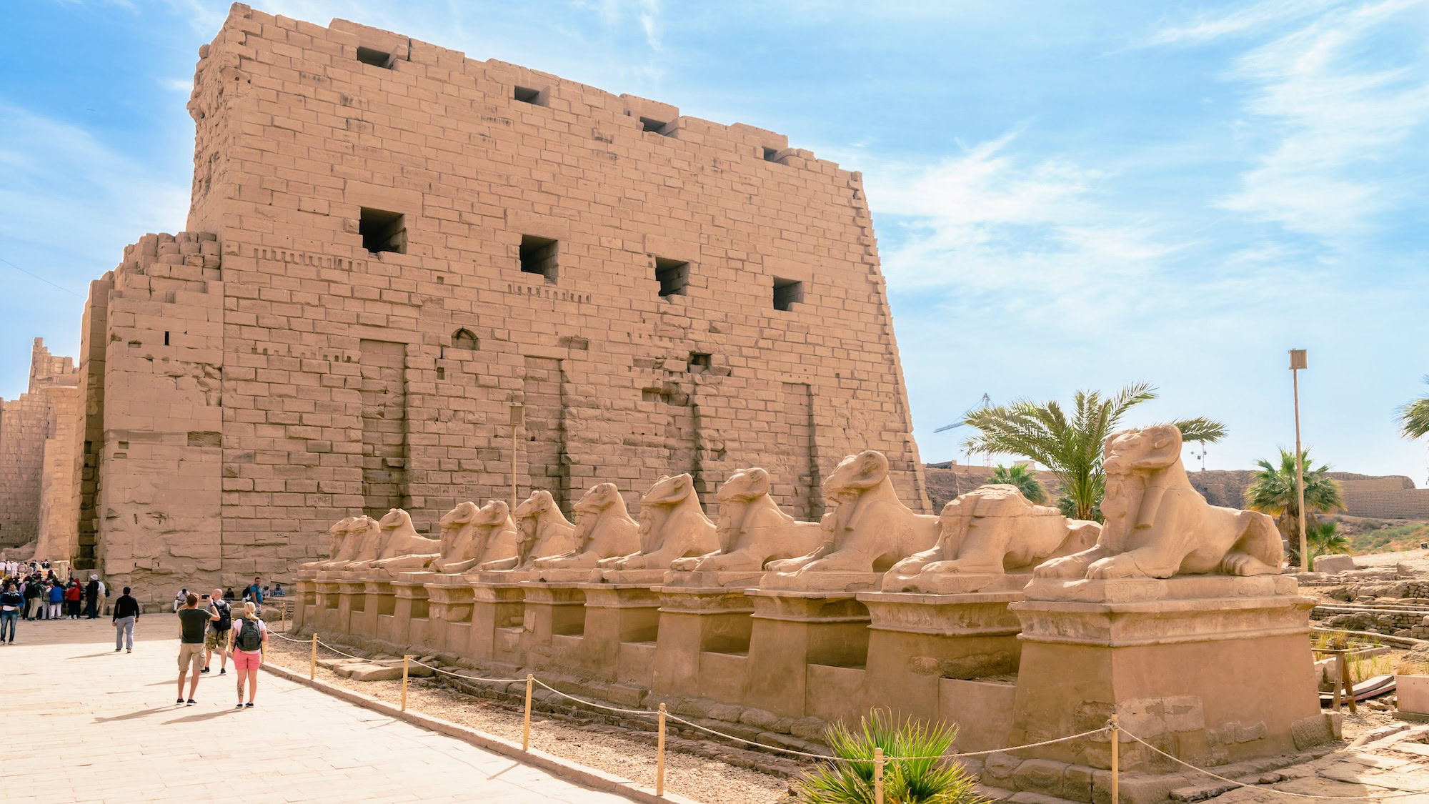 Tourists exploring Karnak Temple Complex with sphinx statues and ancient stone entrance pylon