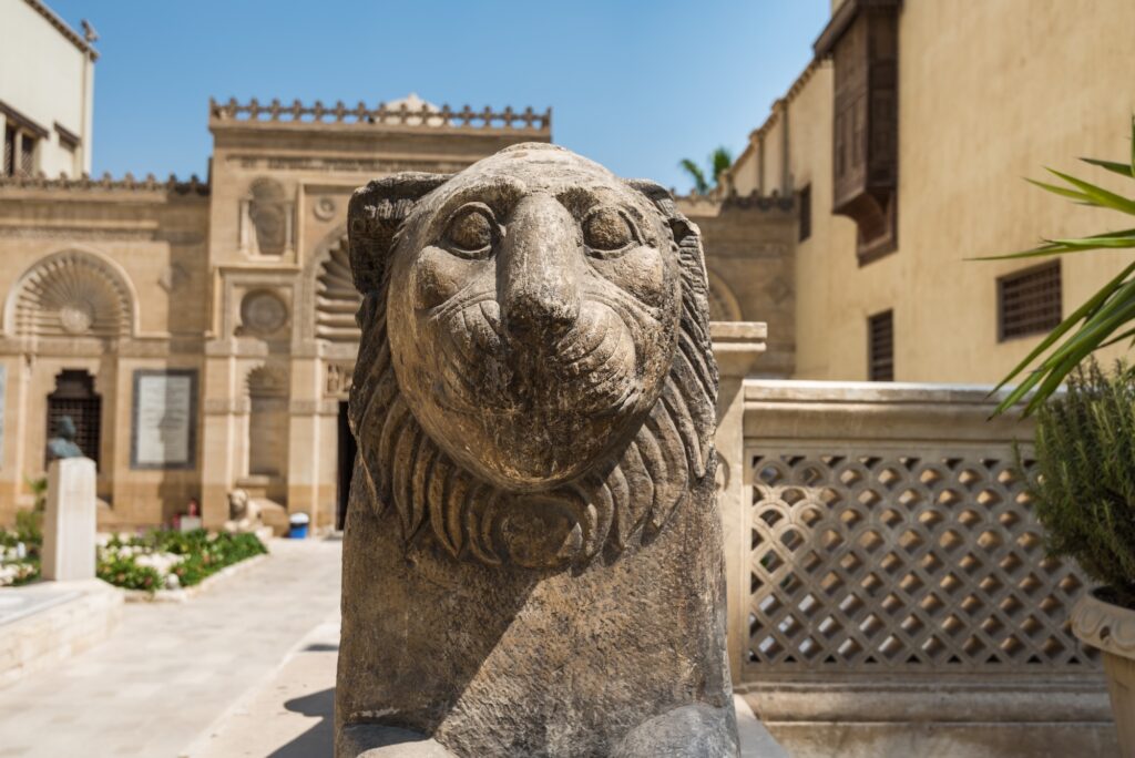 A stone lion statue positioned at the entrance courtyard of the Coptic Museum within the historic religious complex, Cairo