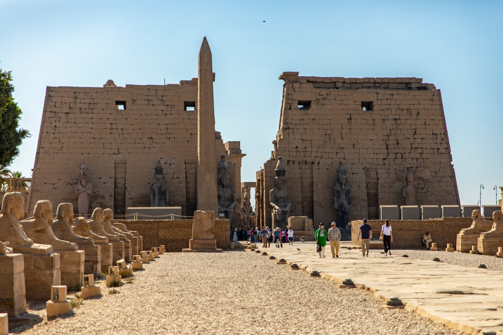 Tourists visiting Luxor Temple with ancient Egyptian obelisk and sphinx statues