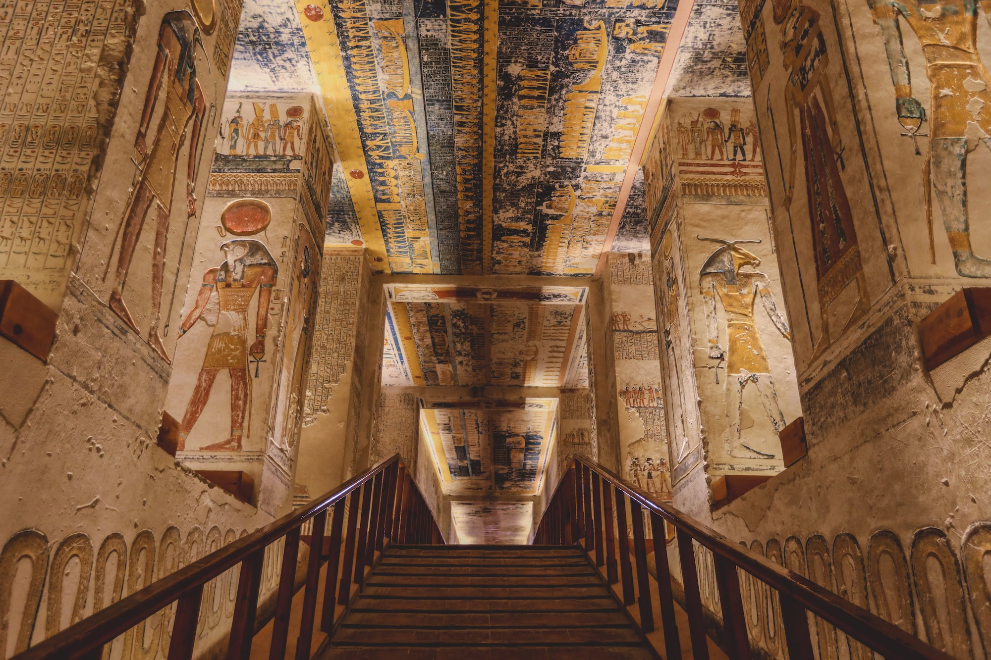 Interior of ancient Egyptian pharaoh tomb showing colorful hieroglyphic wall paintings and decorated ceiling