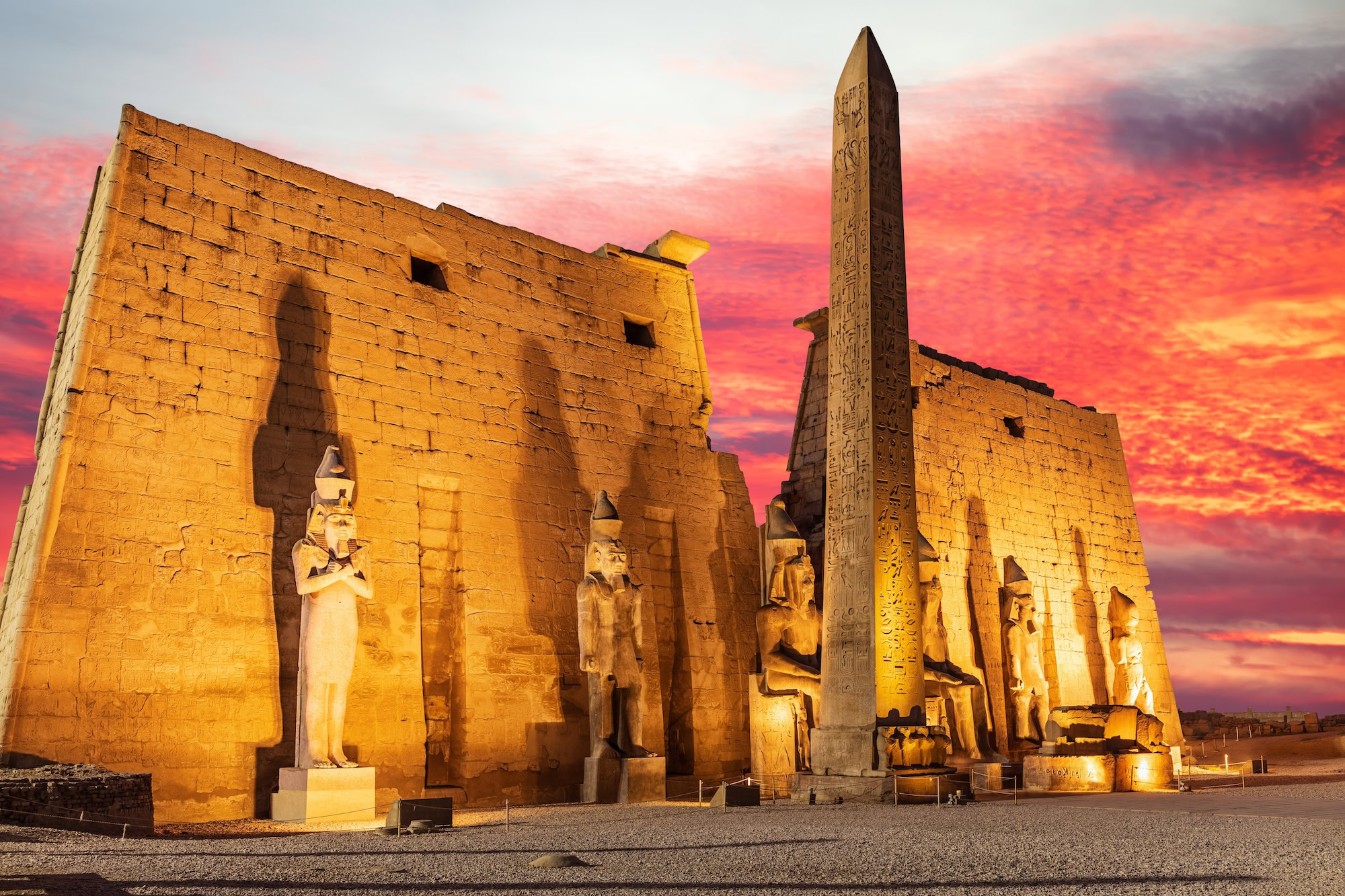 Luxor Temple with obelisk, pharaoh statues and hieroglyphs under sunset sky