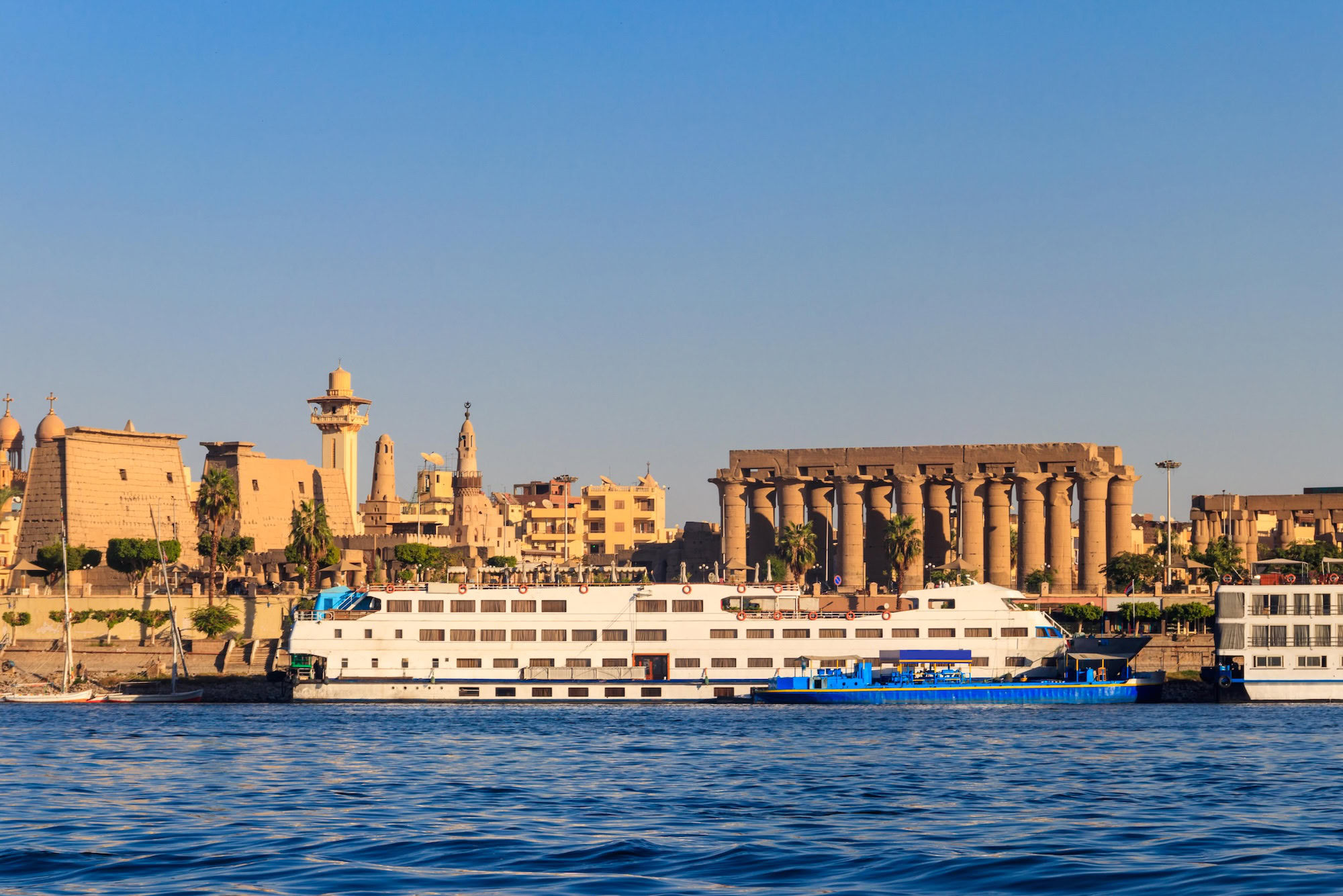 Luxury cruise ship on the Nile River near ancient Luxor Temple with palm trees