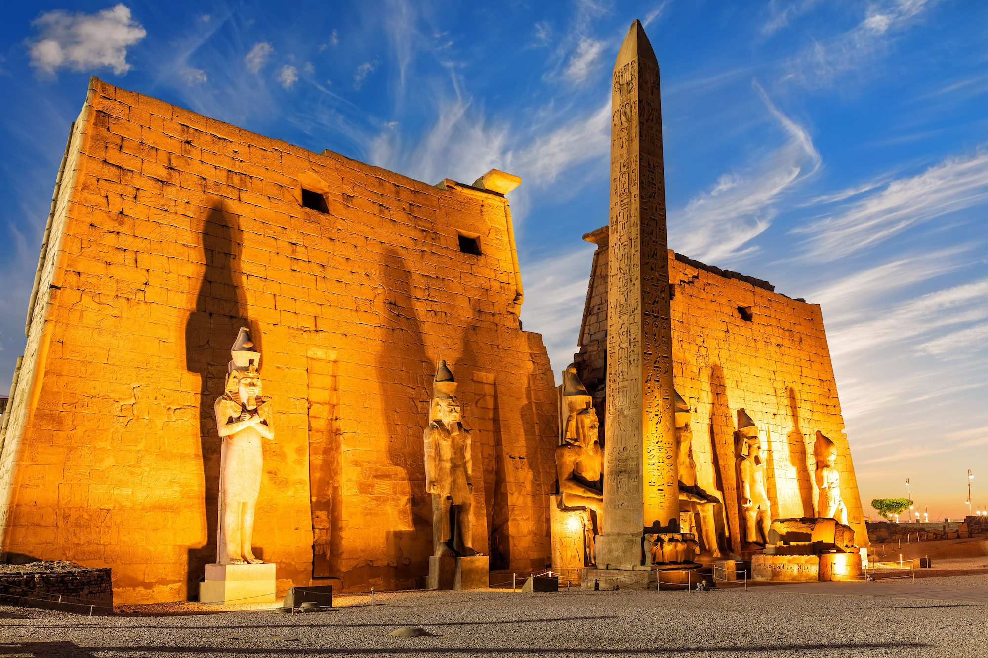 Luxor Temple with towering obelisk, ancient columns, hieroglyphics and pharaoh statues against cloudy sky