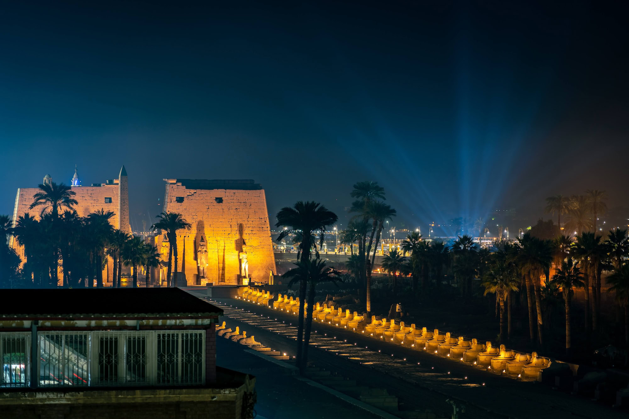 Luxor Temple illuminated with golden lights during evening light show against blue sky
