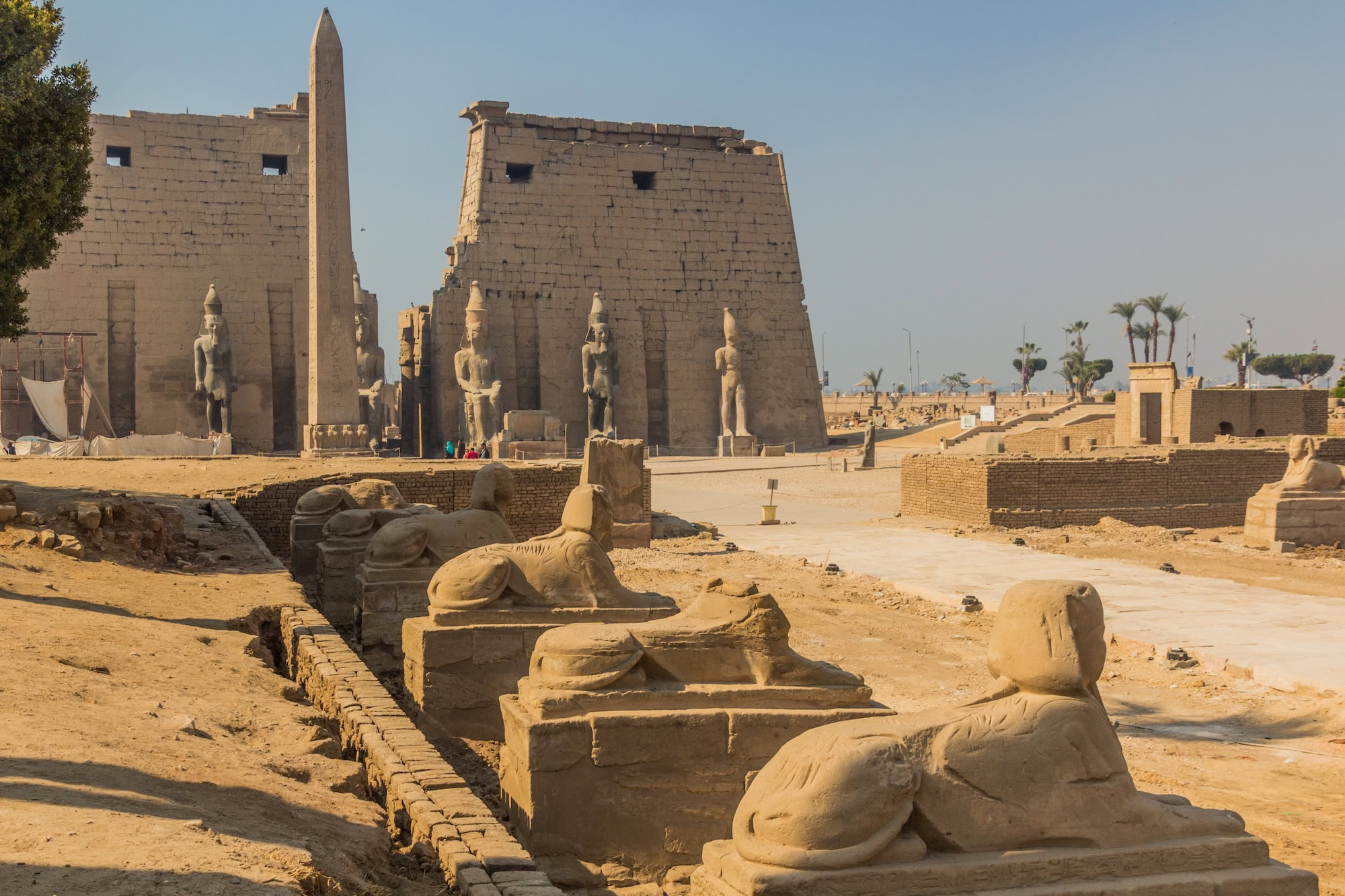 Ancient Luxor Temple complex with sphinx statues, obelisk, and visitors exploring archaeological ruins