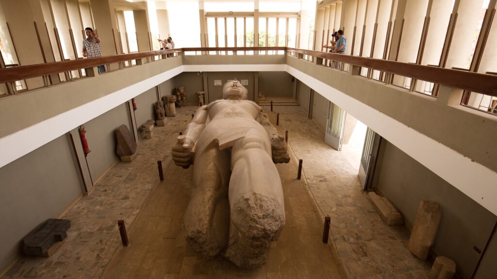 Tourists observing the massive limestone colossus of King Ramses II displayed in the open-air museum at Memphis, Memphis