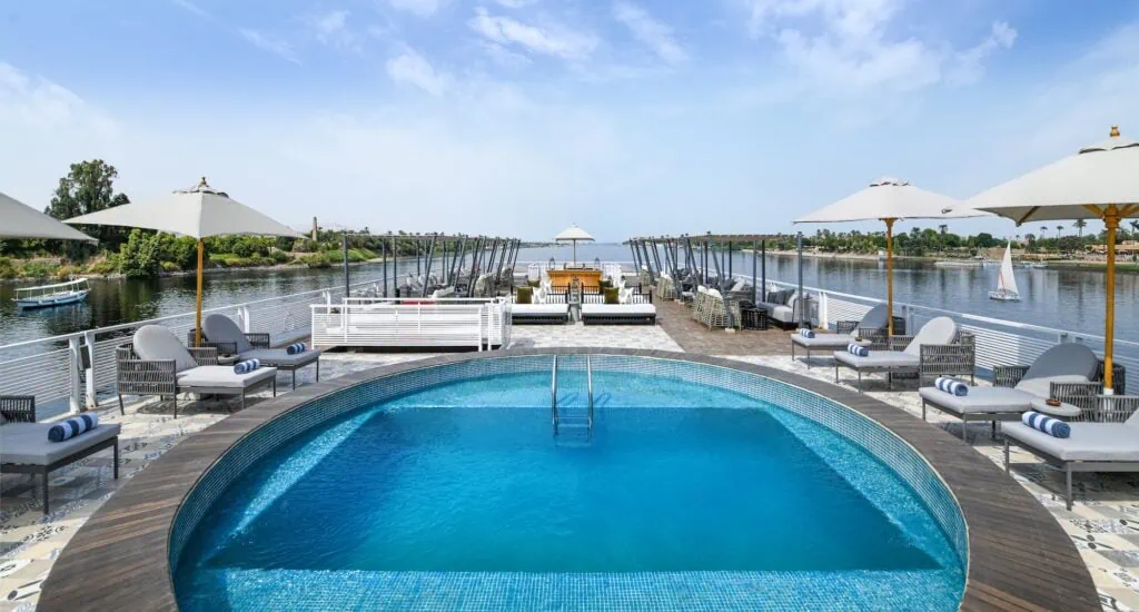 The sun deck and swimming pool aboard the Mövenpick MS Darakum, with lounge chairs arranged around the pool and a wide view of the Nile River from the upper deck.