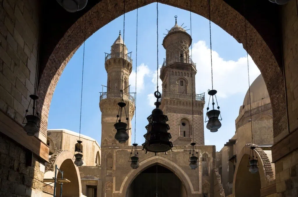 Large stone arch framing views of the minarets of the Madrasa of Al-Nasir Muhammad and the Qalawun Complex along Al-Muizz Street