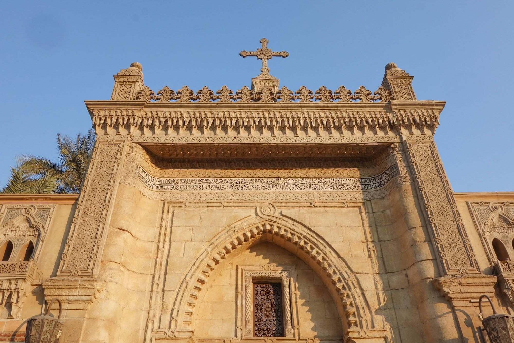 Ancient Coptic church facade with carved stone columns, arched entrance, and ornate decorative stonework