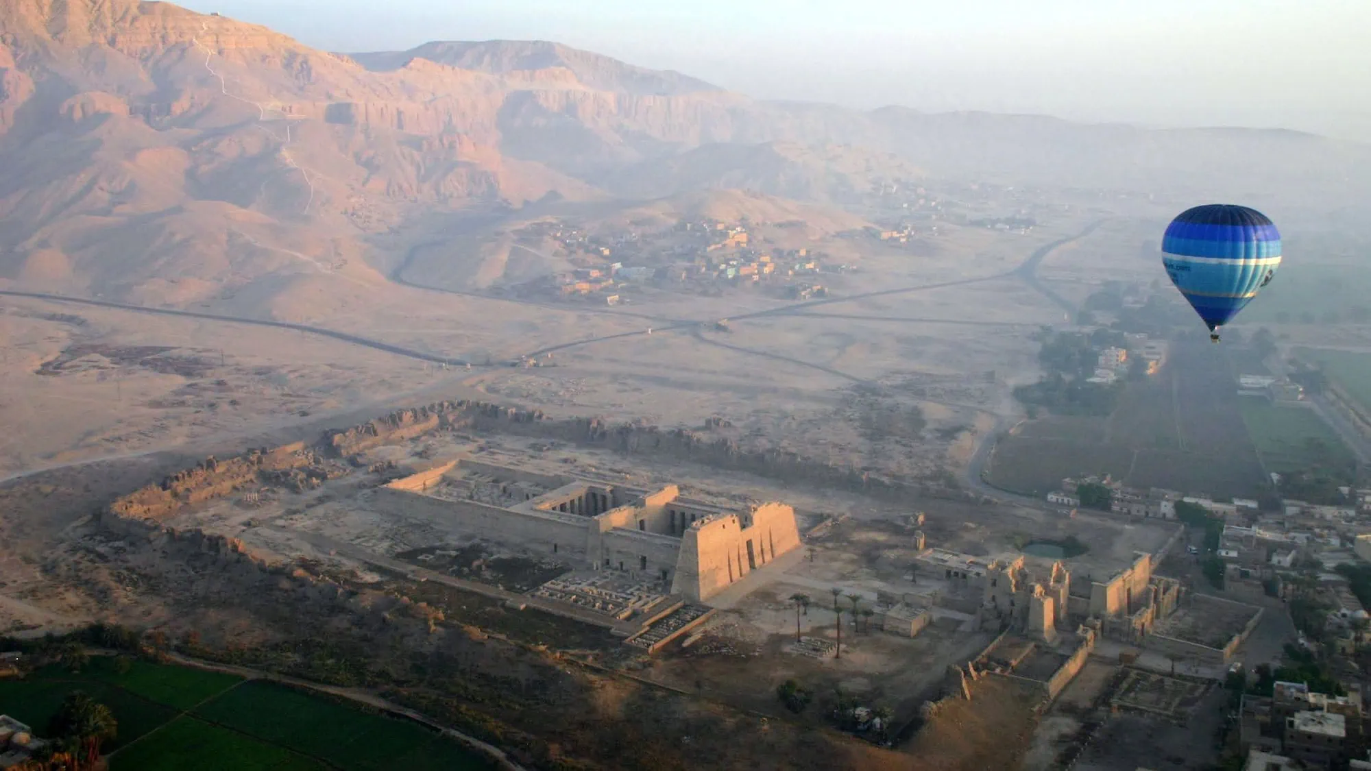 Hot air balloon floating over ancient temples and archaeological ruins in Valley of the Kings