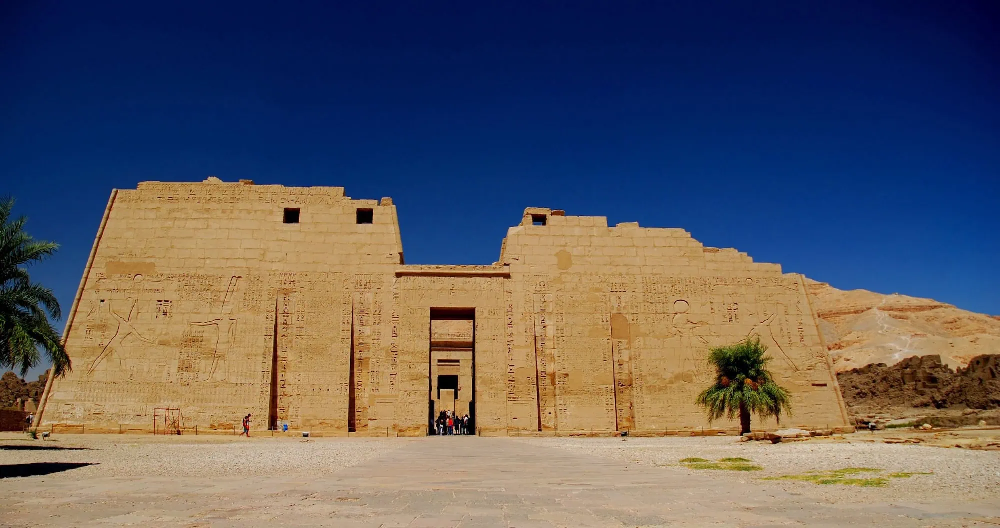 Turistas visitando el templo de Medinet Habu con palmeras y jeroglíficos