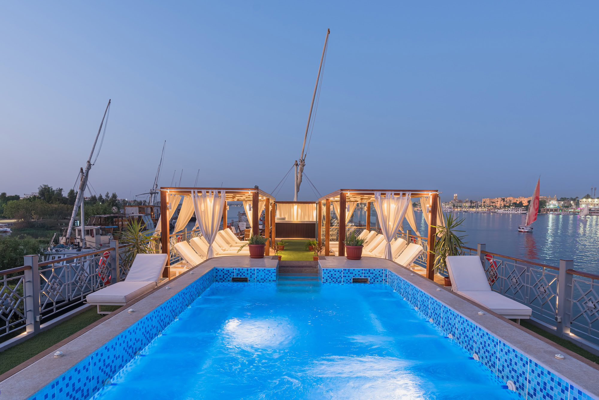 Luxurious Nile River cruise ship pool deck with traditional felucca sailboats on the river