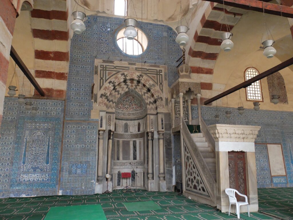 The mihrab with blue tile decoration and the carved wooden minbar inside Aqsunqur Mosque, Cairo