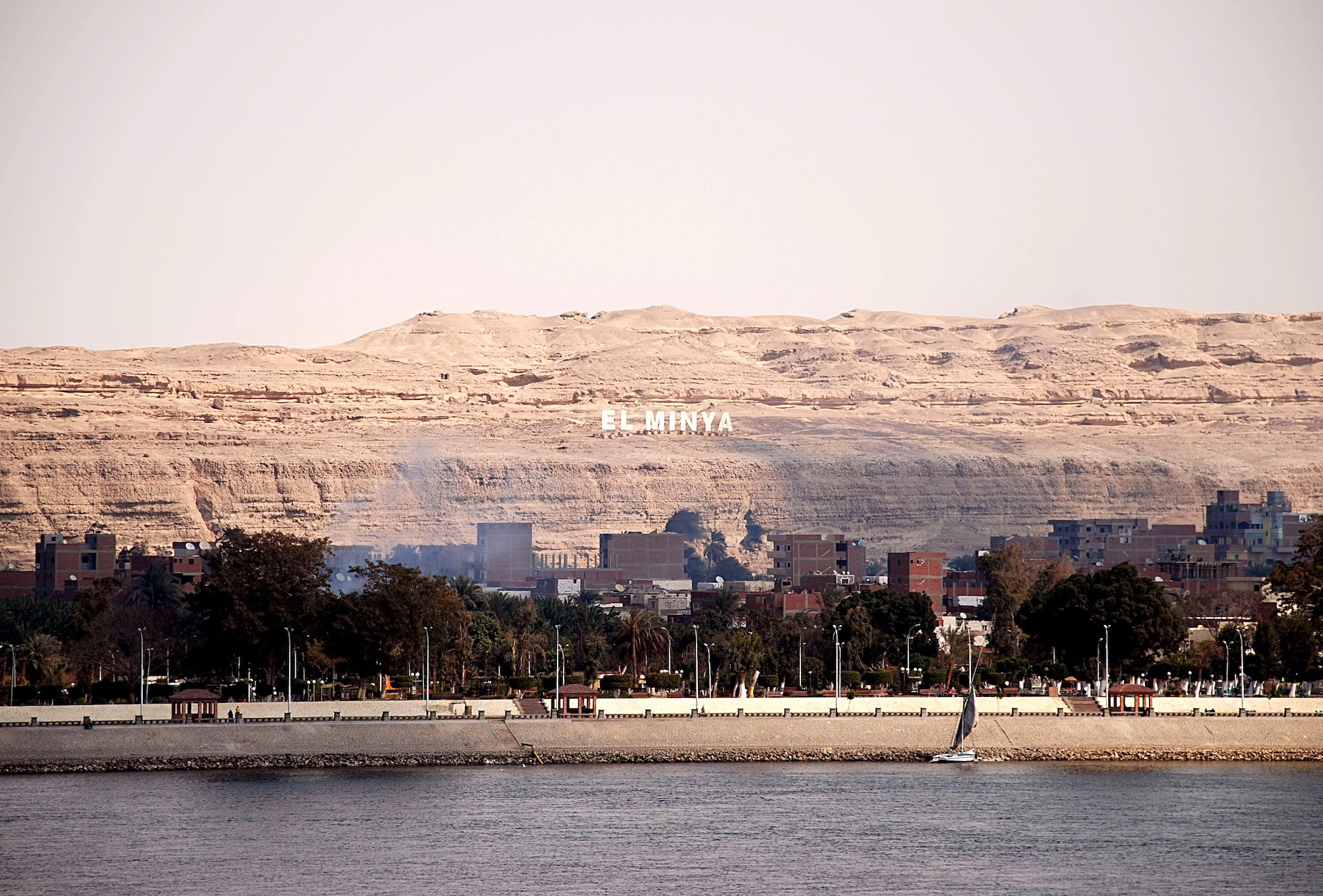 Minya waterfront with sailboat on river, palm trees and cliffs