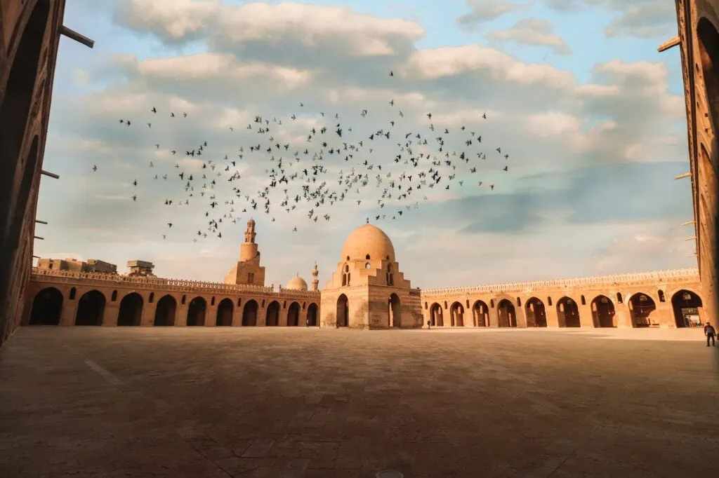 A wide view of the open courtyard with stone paving, surrounding arcades, and the central ablution fountain at the Ibn Tulun Mosque, Cairo