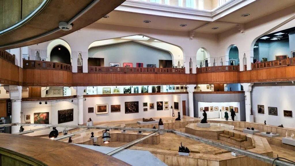 An interior gallery view with modern paintings, sculptures, display platforms, and seating inside the Museum of Modern Art, Cairo