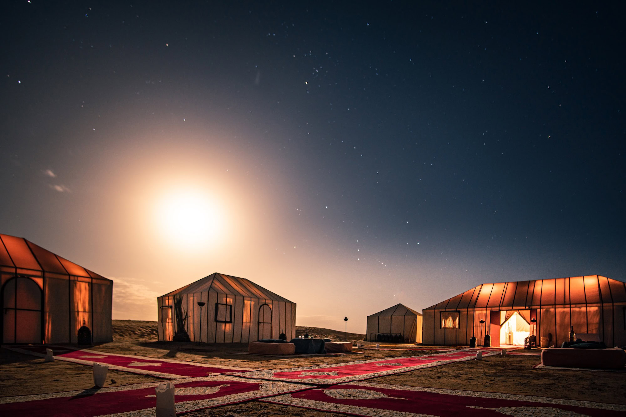 Desert camping tents under a starry night sky with moon visible