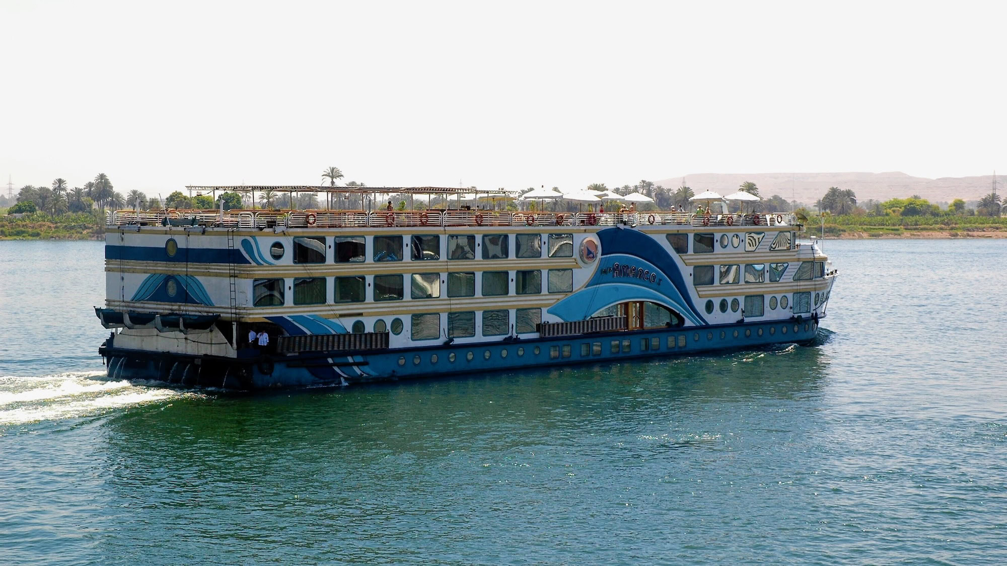 Nile River cruise boat with palm trees and desert hills in Egypt