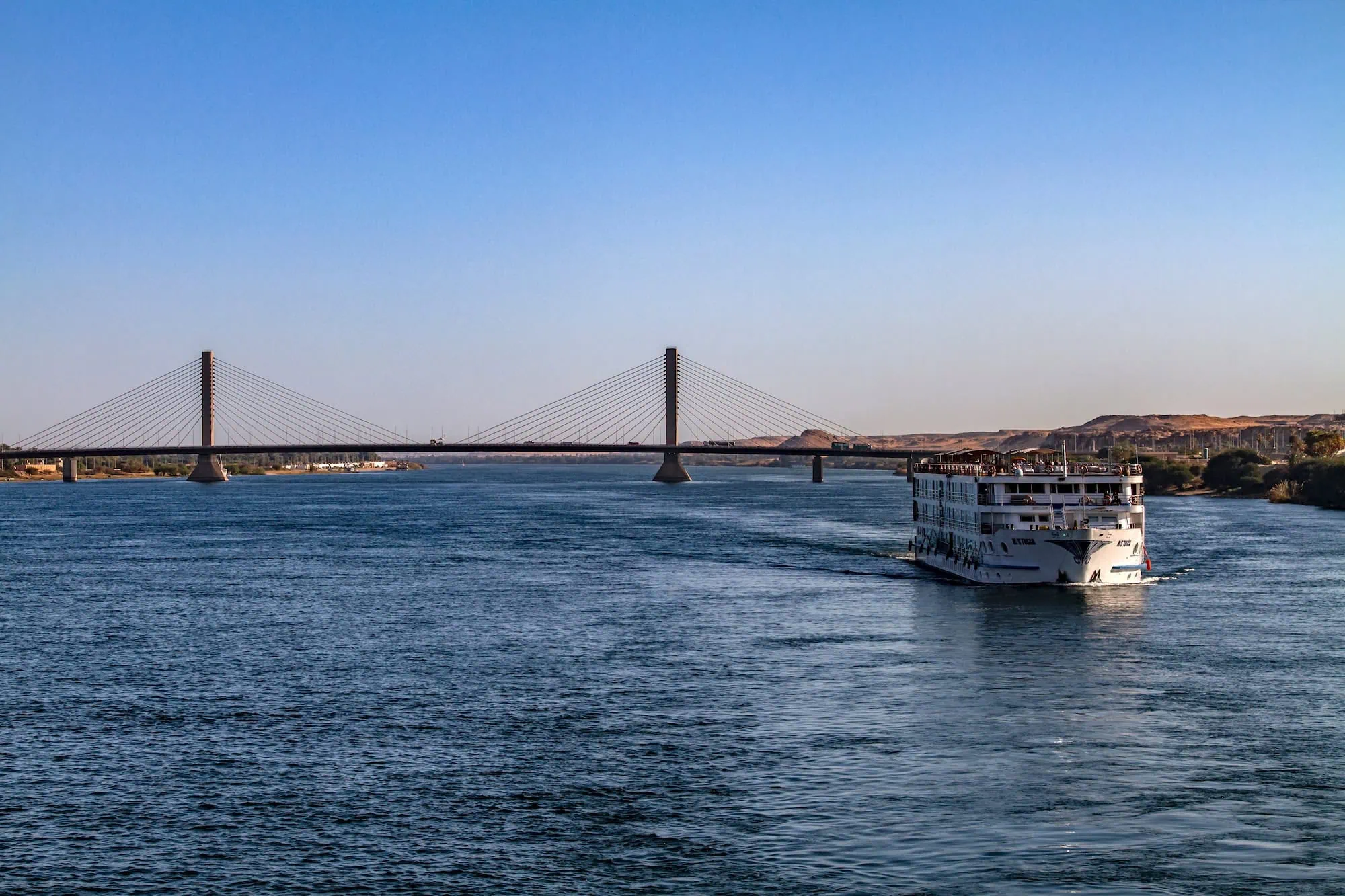 Cruise ship sailing on the Nile River in Aswan with modern cable bridge in background