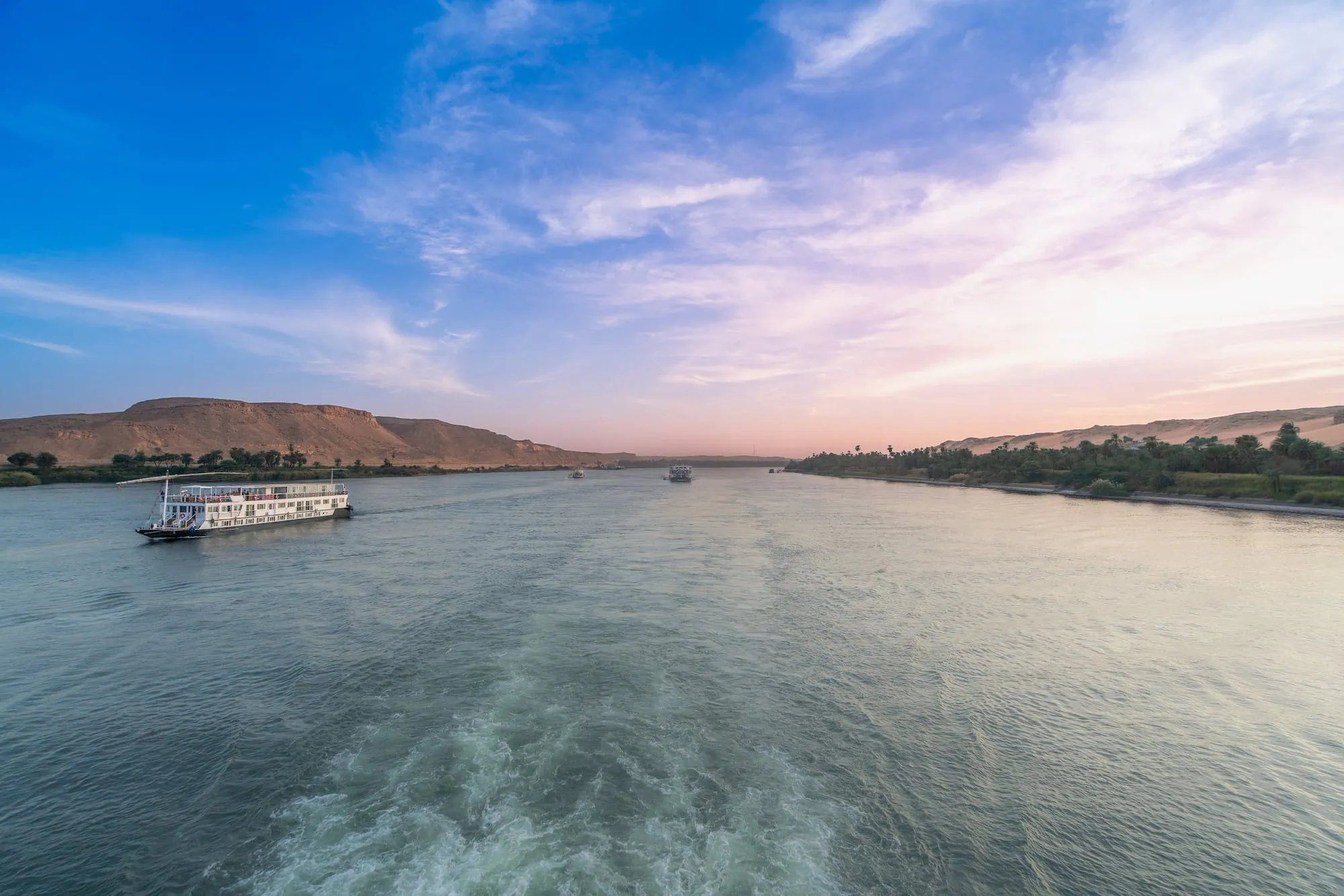 Two white cruise boats sailing on the Nile River at sunset near Aswan, Egypt