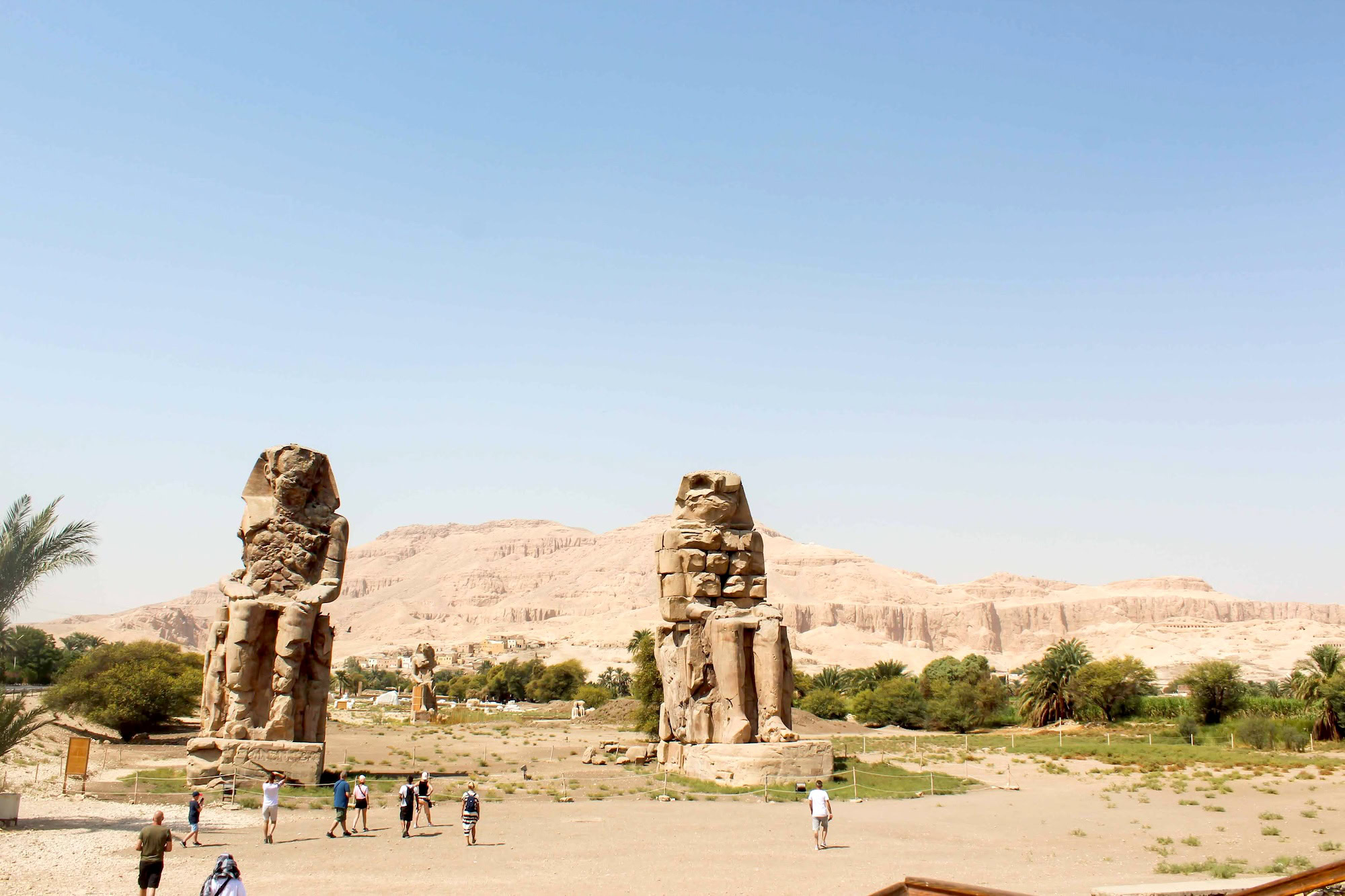 Two massive ancient stone statues of Colossi of Memnon with tourists nearby