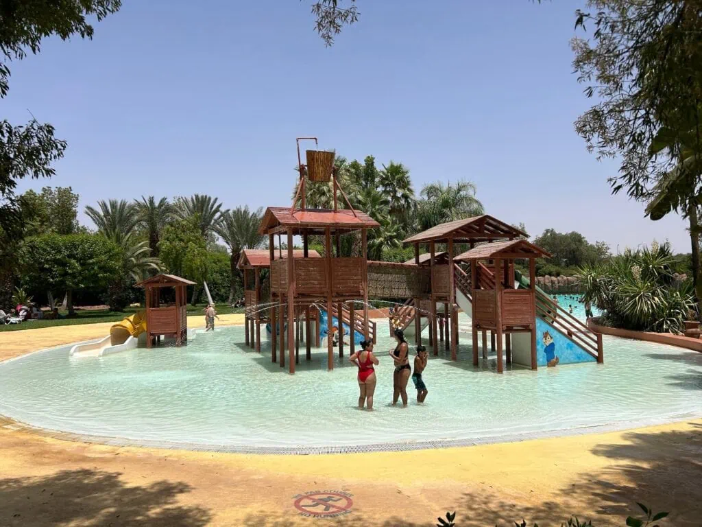 Oasiria water park with shallow pool, wooden play structures, slides, and visitors in the water Marrakech