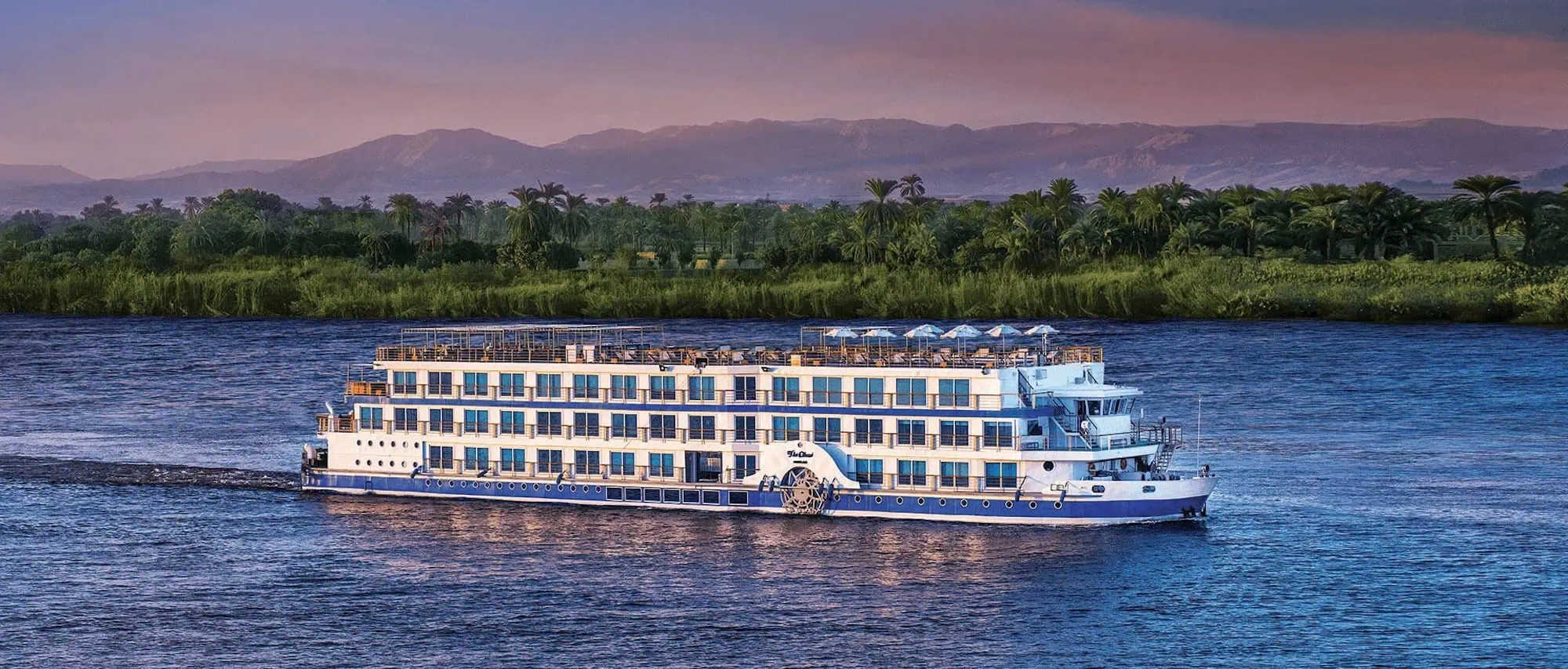 Nile River cruise ship with hotel accommodations surrounded by palm trees and mountains