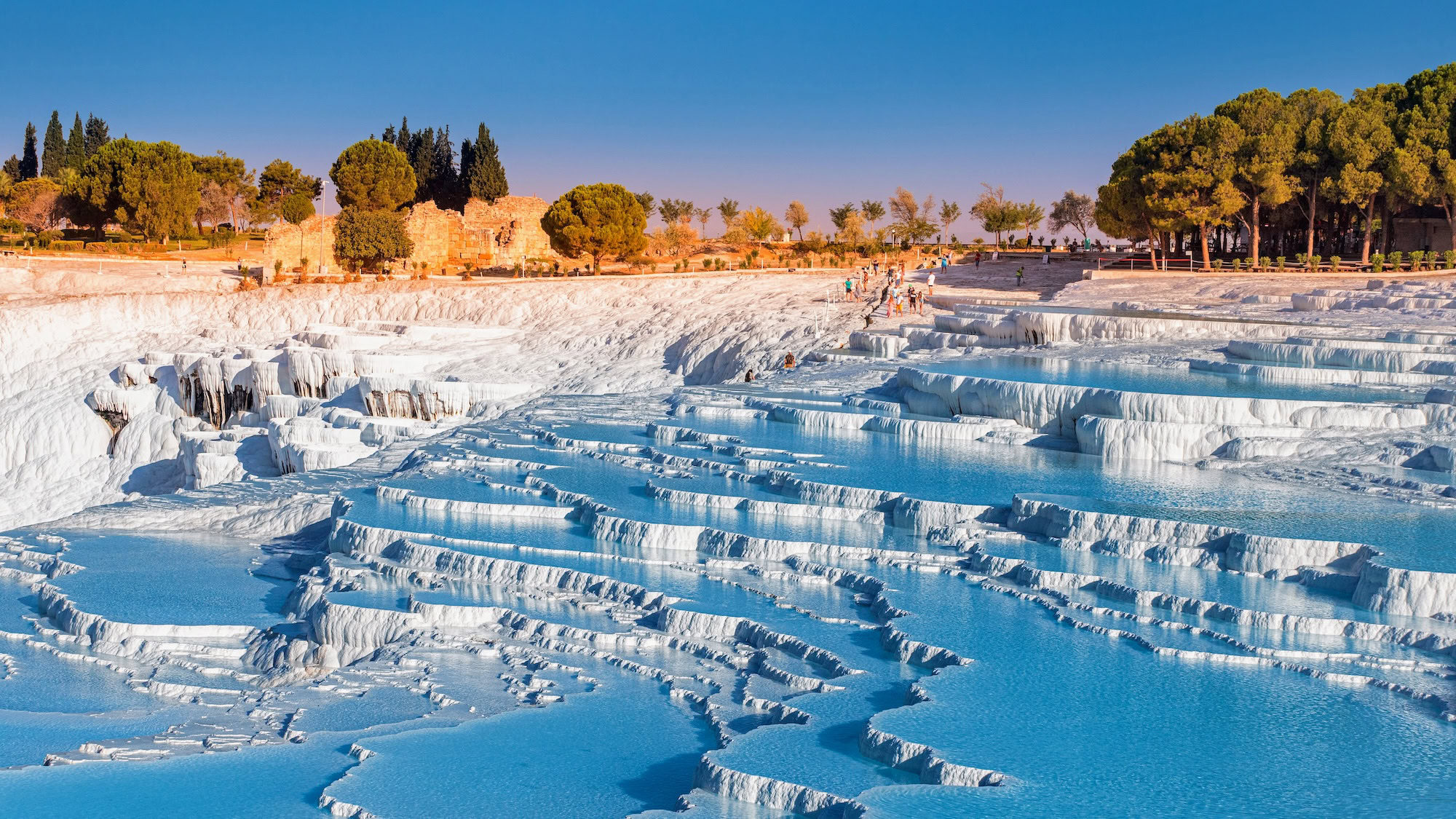 Pamukkale's white travertine terraces with thermal pools and ancient ruins visible in the background
