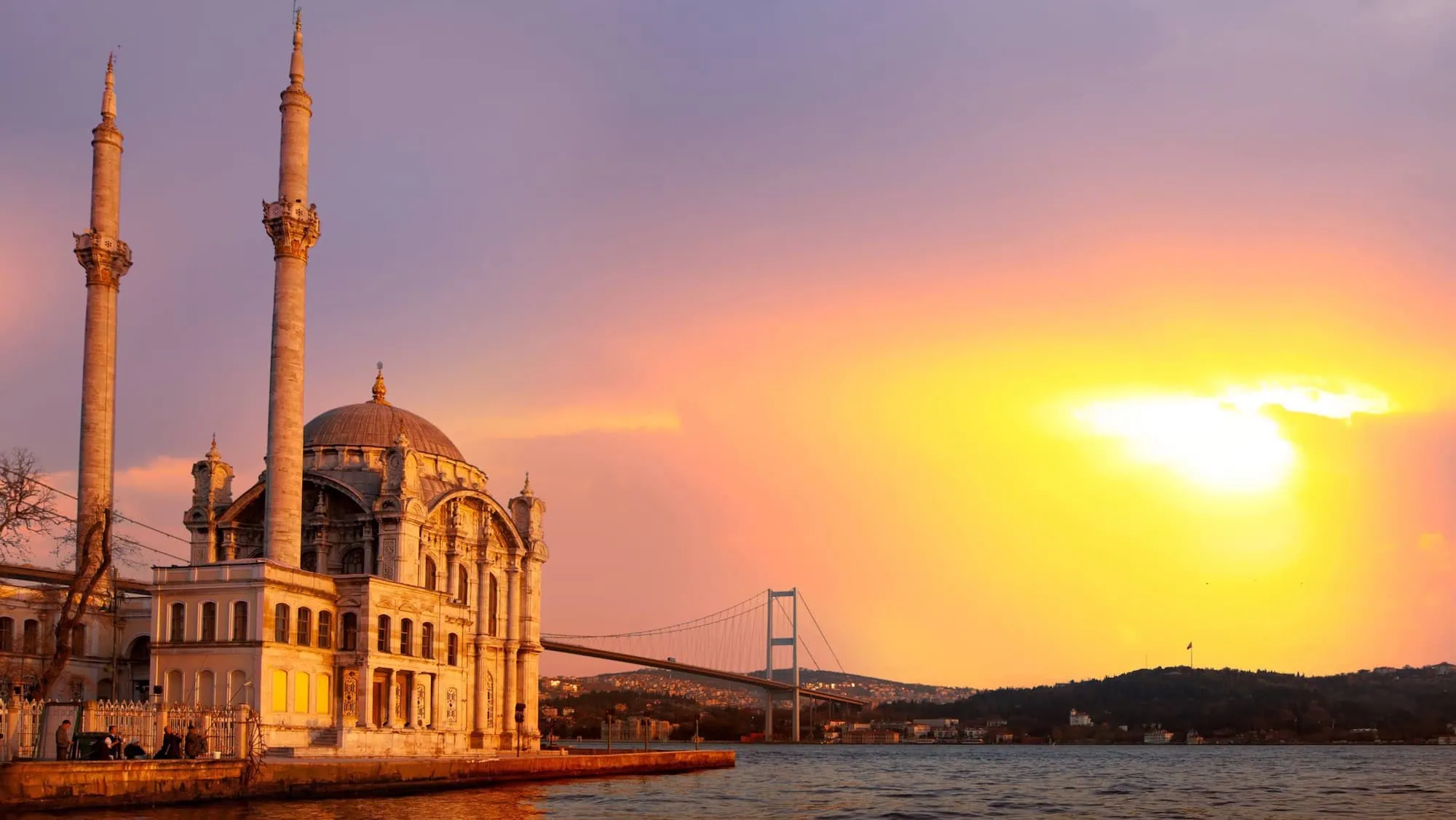Ortakoy Mosque with twin minarets at sunset with Bosphorus Bridge spanning the water in background