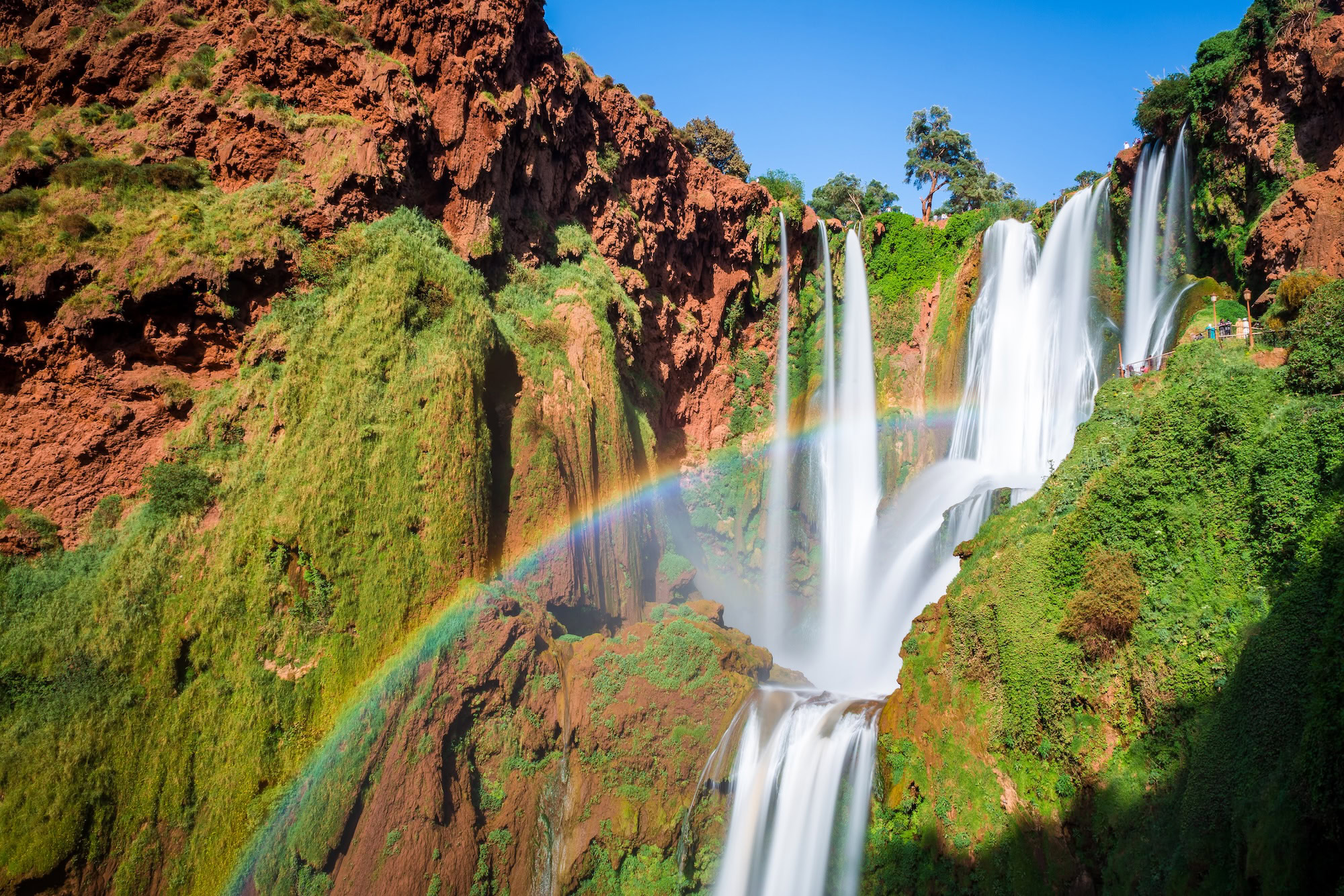 Spectacular Ouzoud Falls waterfall with rainbow, lush vegetation and dramatic cliffs in Morocco