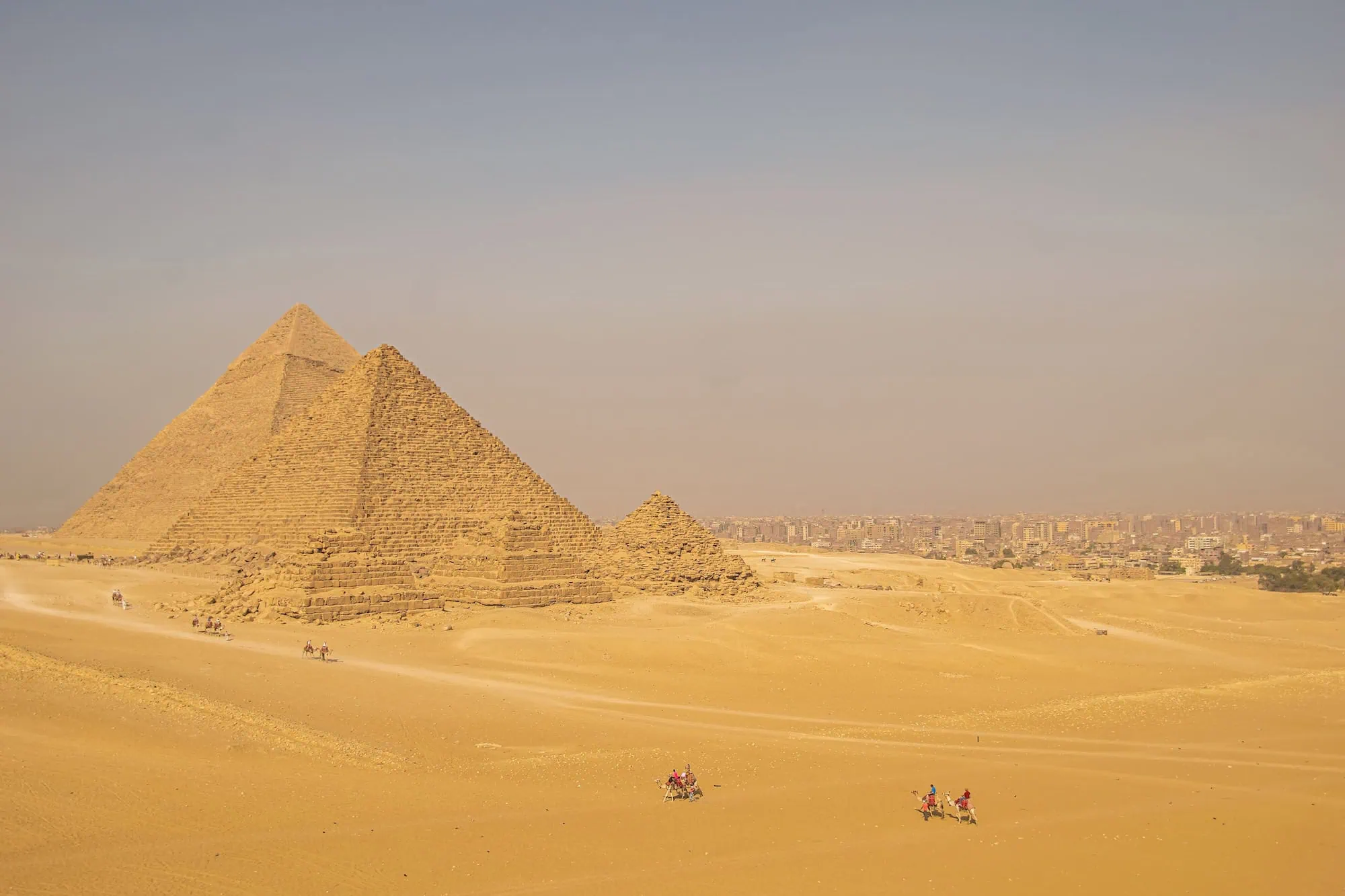 Panoramic view of Giza pyramids with small tourist groups and camels in foreground