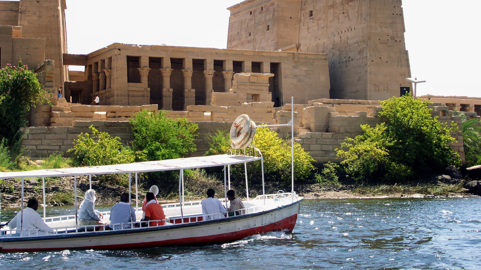 Ancient Philae Temple columns rising from water with tourist boat nearby