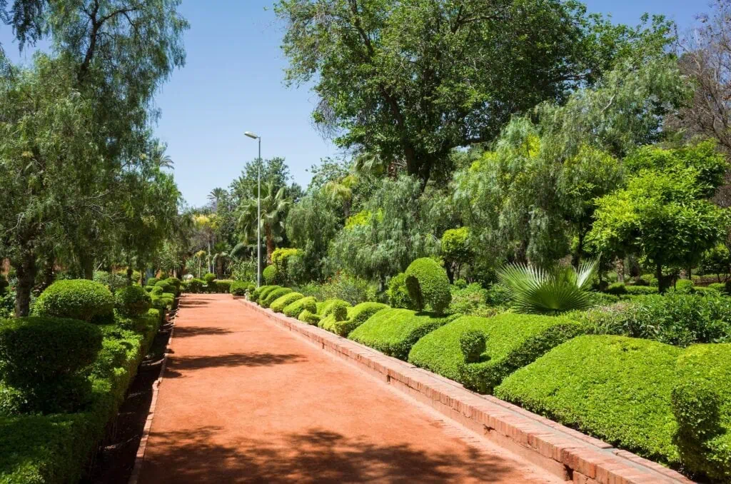 Cyber Park Arsat Moulay Abdeslam pathway lined with trees and dense greenery along a red earthen trail Marrakech