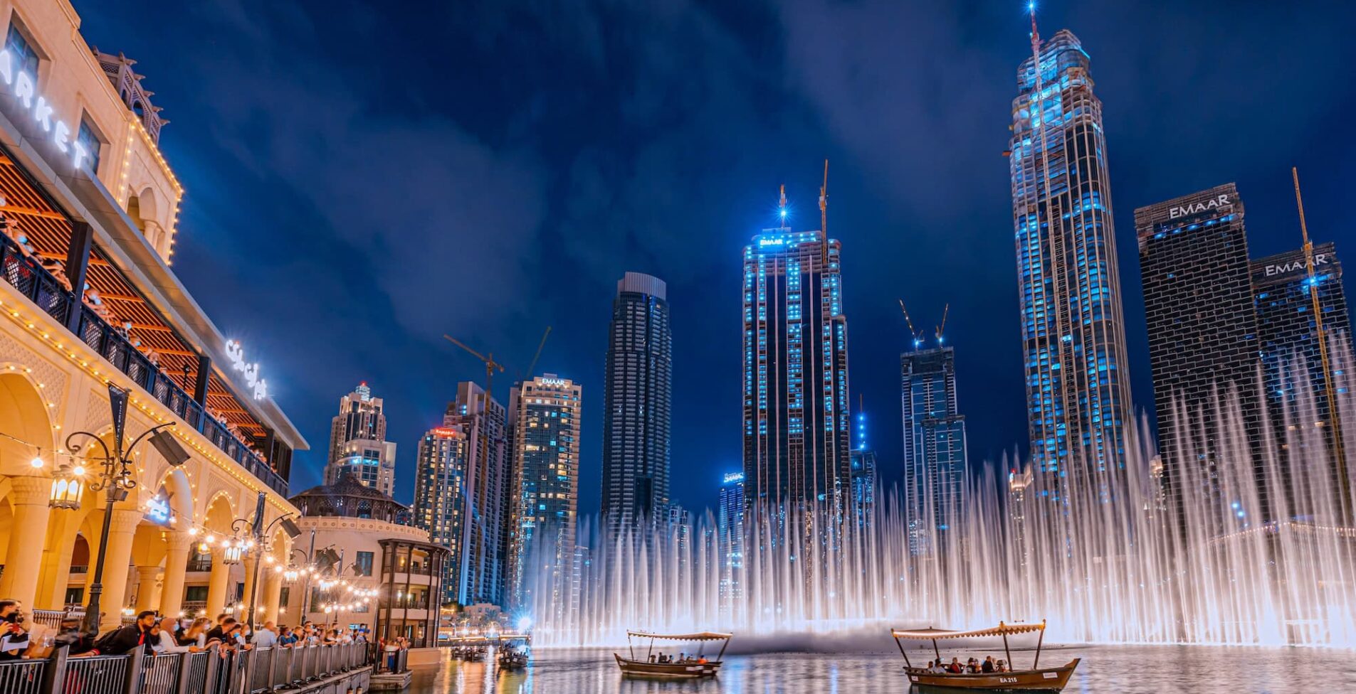 People enjoy a boat ride while watching a performance of the Dubai Fountain at night with the skyscrapers of Dubai in the background