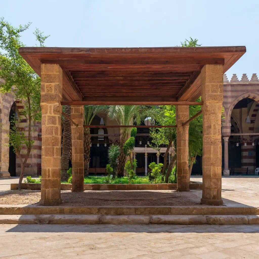 A courtyard pergola supported by four stone columns with a flat wooden ceiling at the Amir Aqsunqur Mosque, Cairo